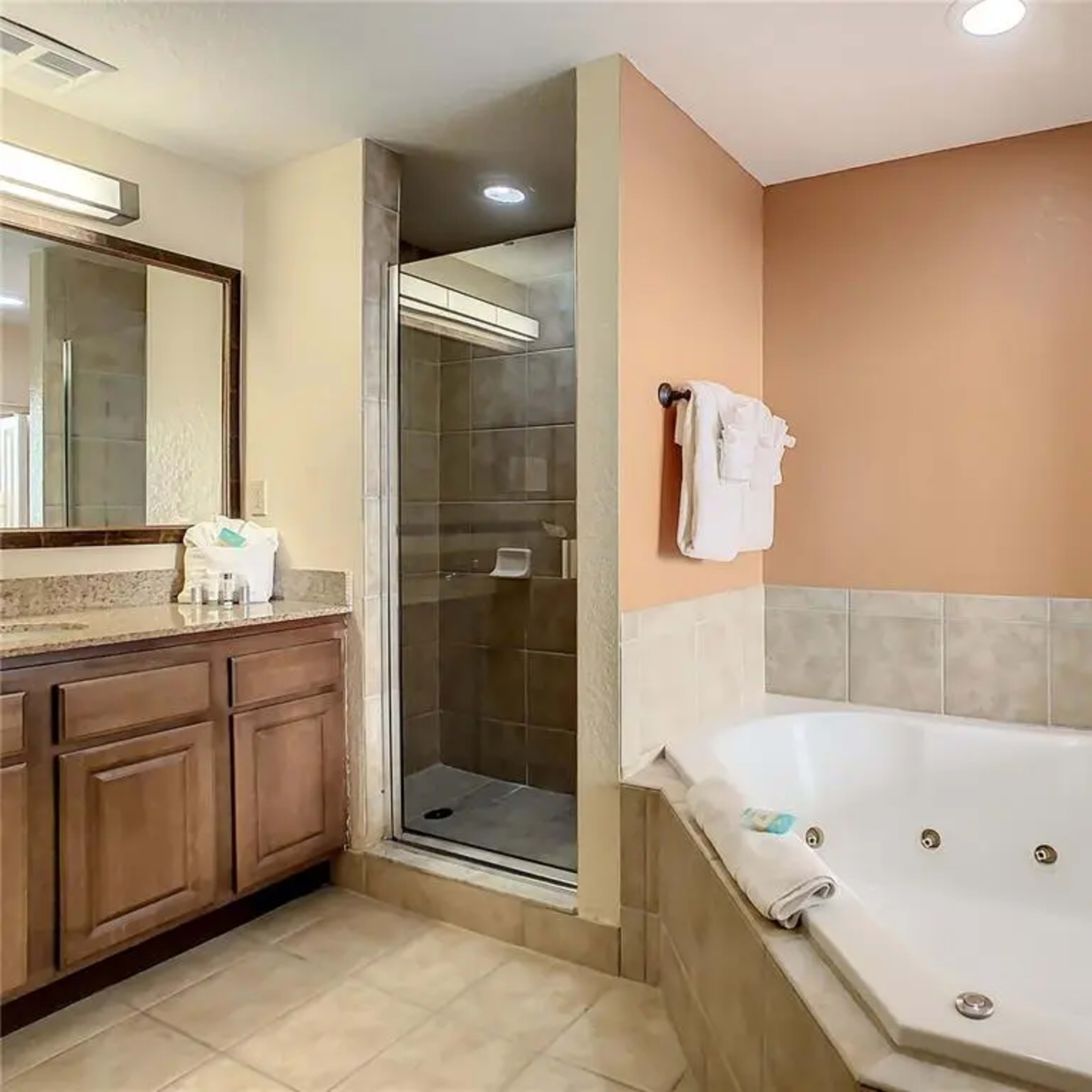 The bathroom features a jetted tub next to a walk-in shower, with a countertop and mirror opposite wooden cabinetry.