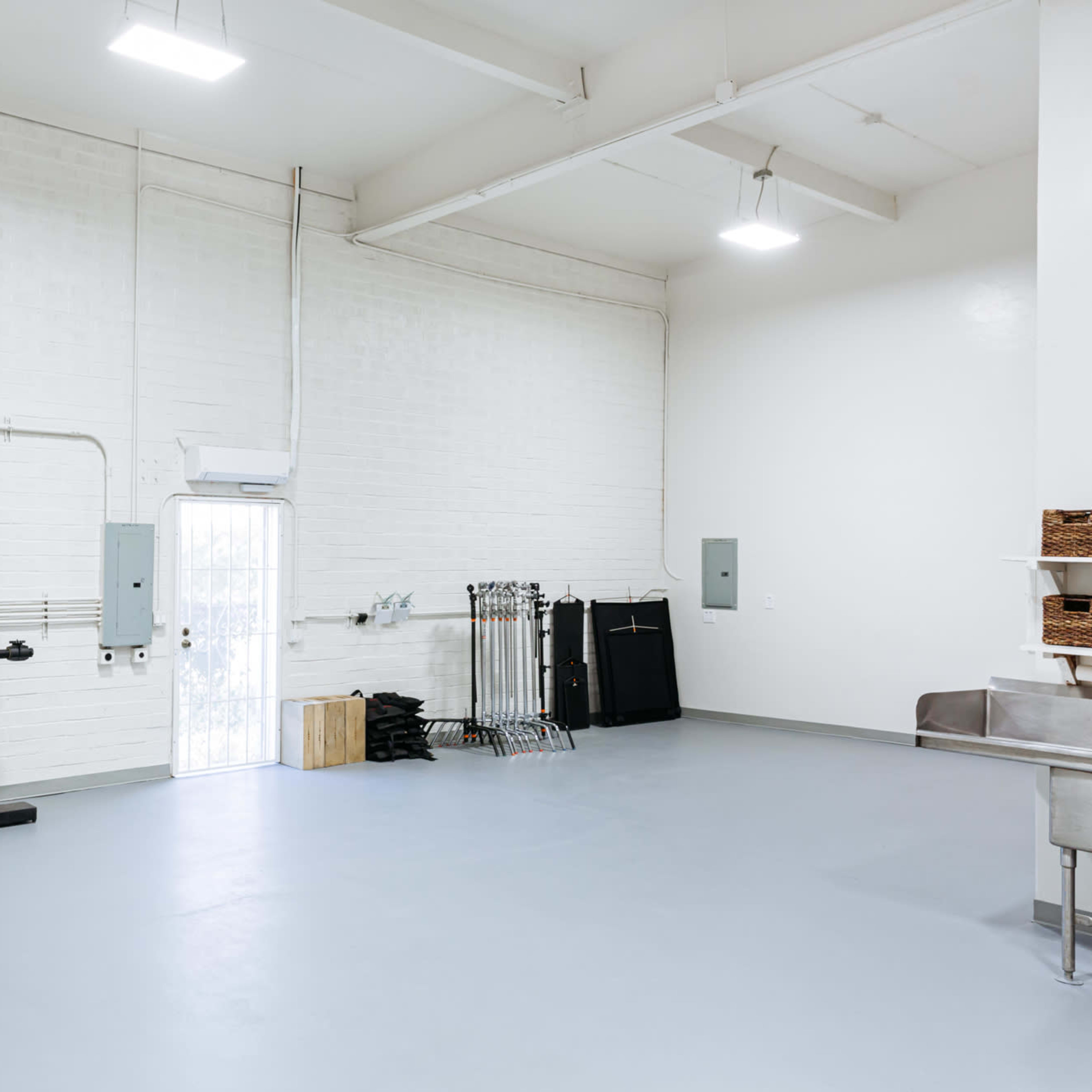 A spacious, empty interior of a room with white brick walls, a light grey floor, and minimal equipment along the sides.