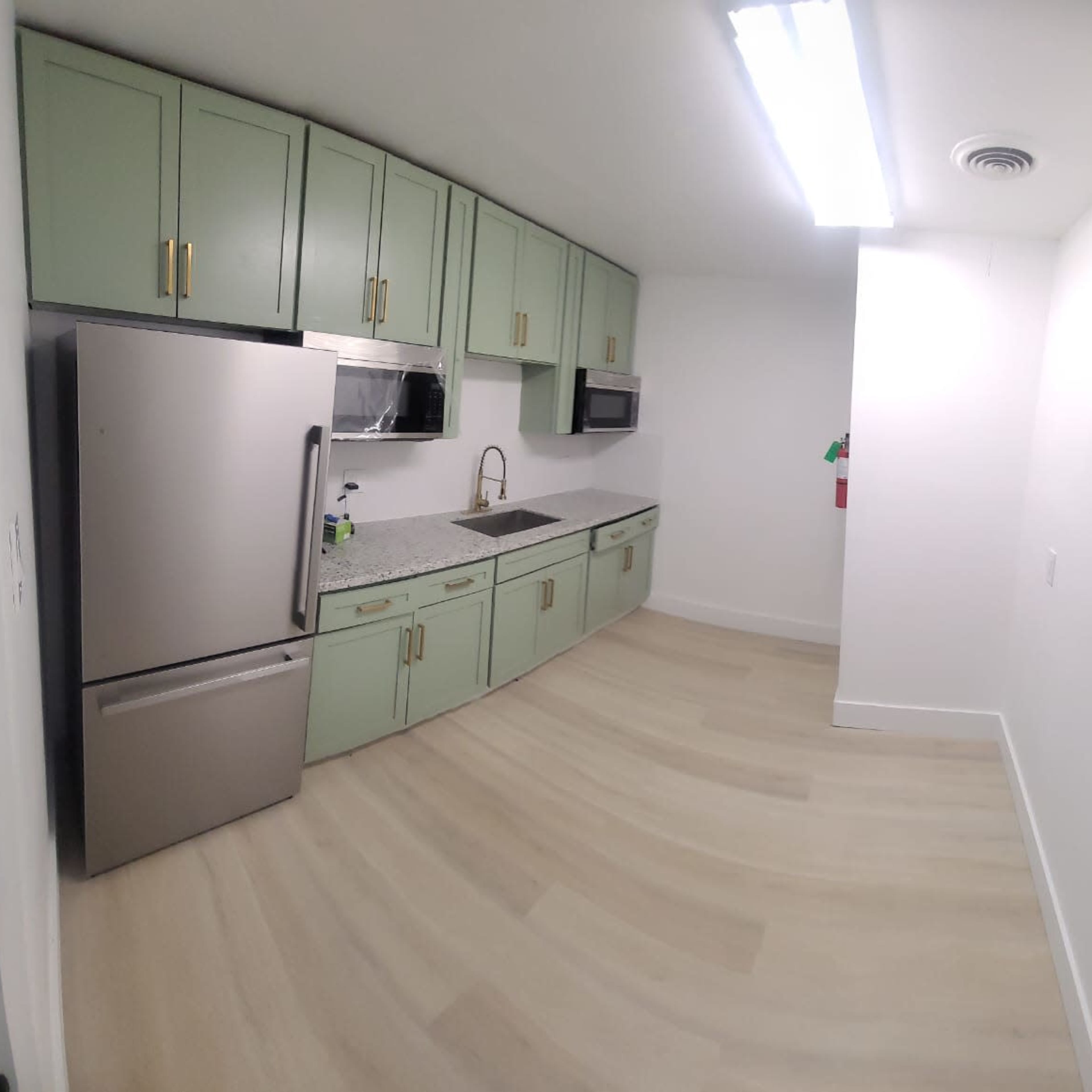 A modern kitchen with light green cabinets, stainless steel appliances, and a countertop with a sink.