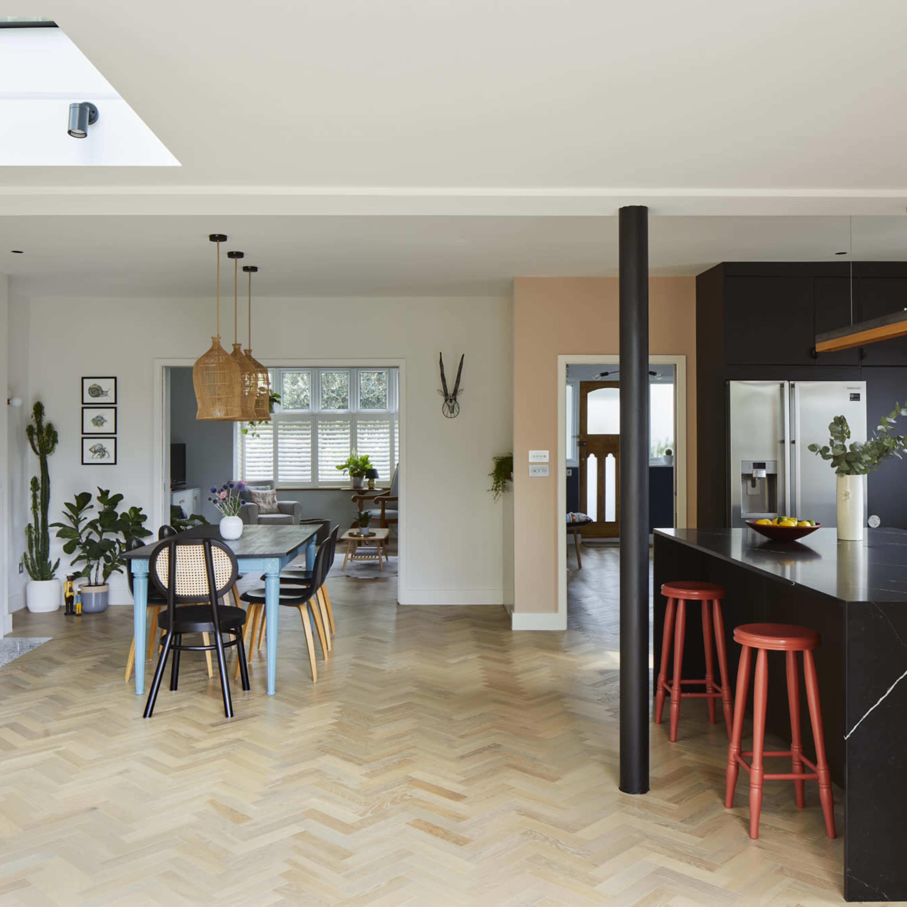A modern kitchen and dining area feature a large island, black cabinetry, a wooden dining table, and various indoor plants.