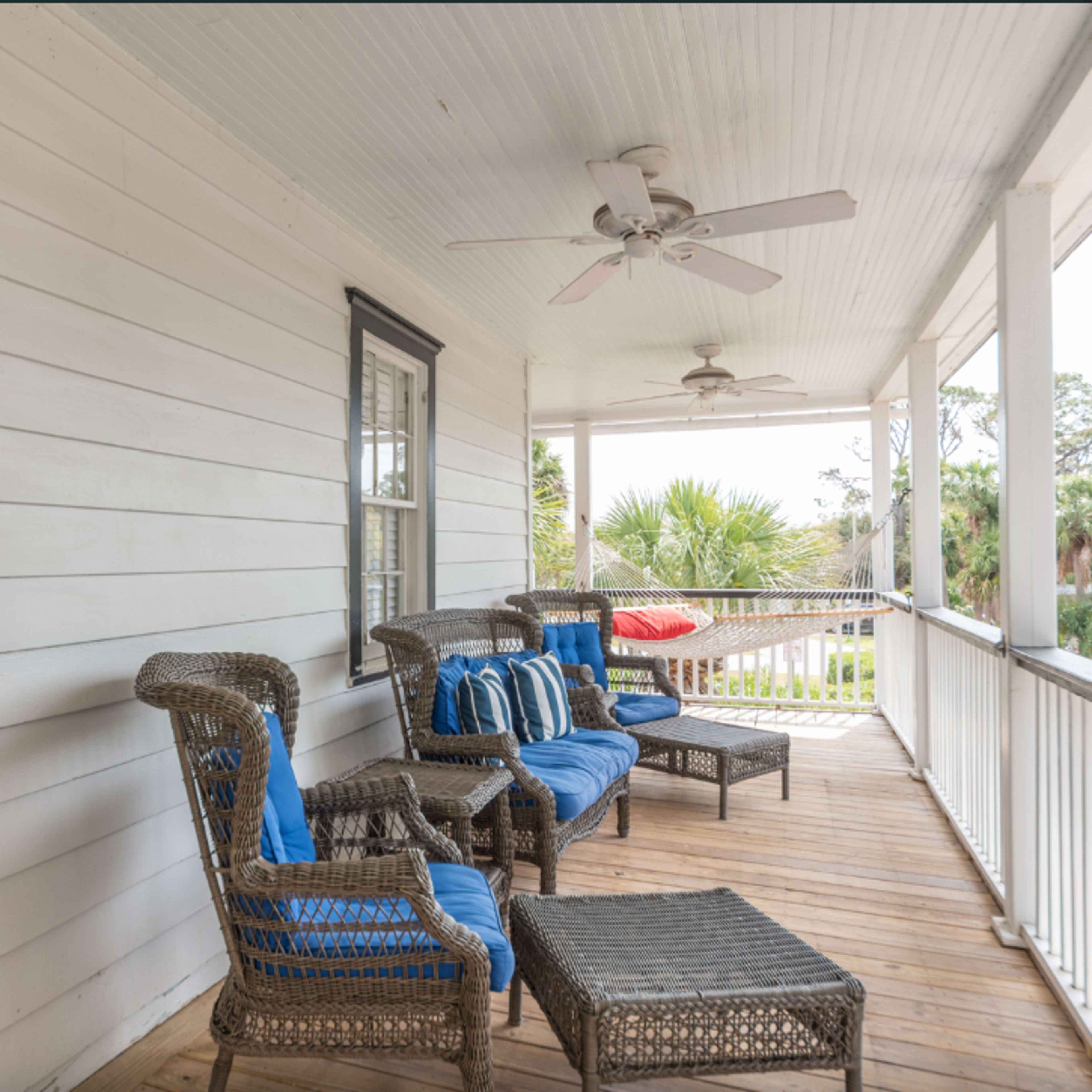 A porch with wicker seating, blue cushions, and a ceiling fan, surrounded by palm trees in the background.