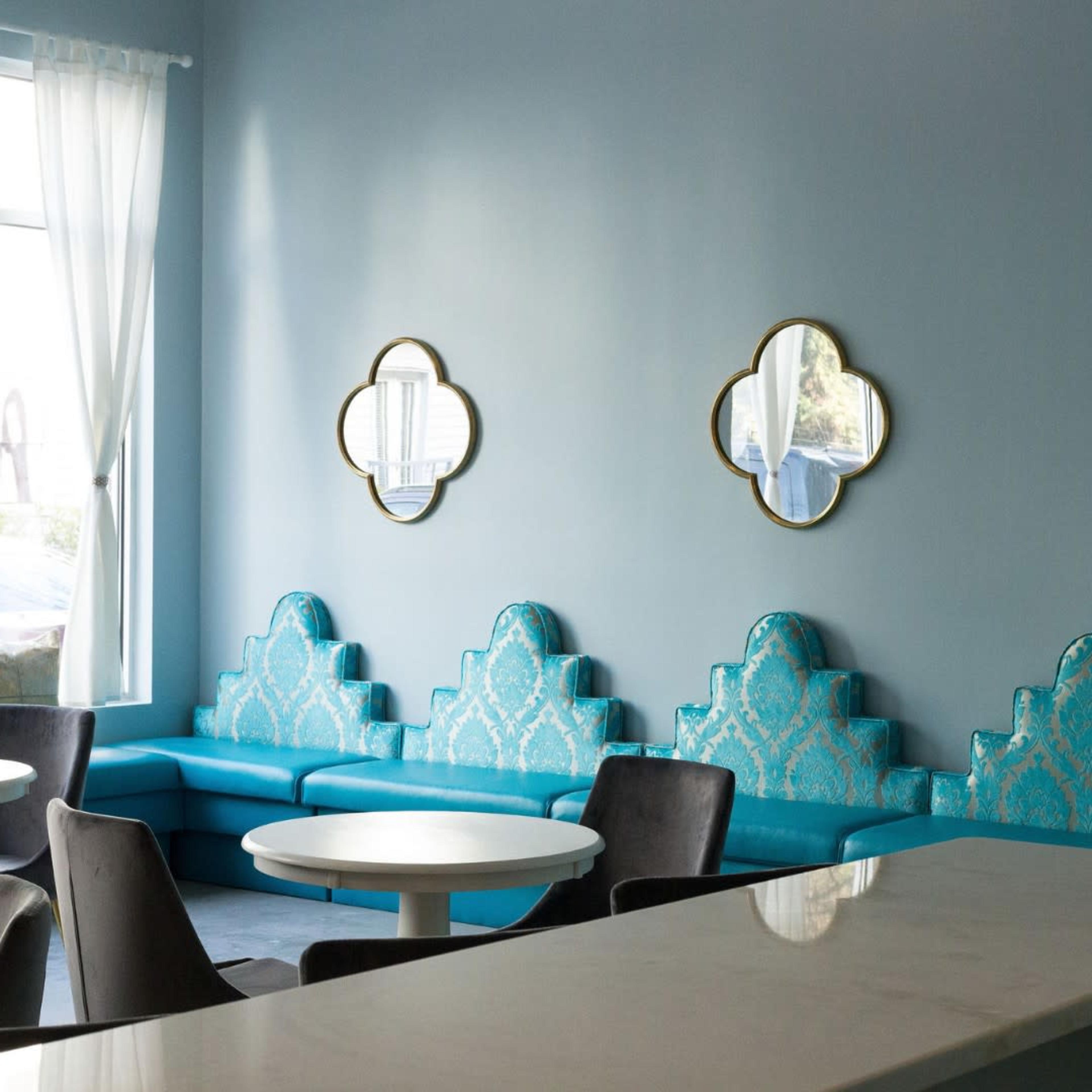 A modern café interior with turquoise seating, three decorative mirrors, and round tables against a light blue wall.