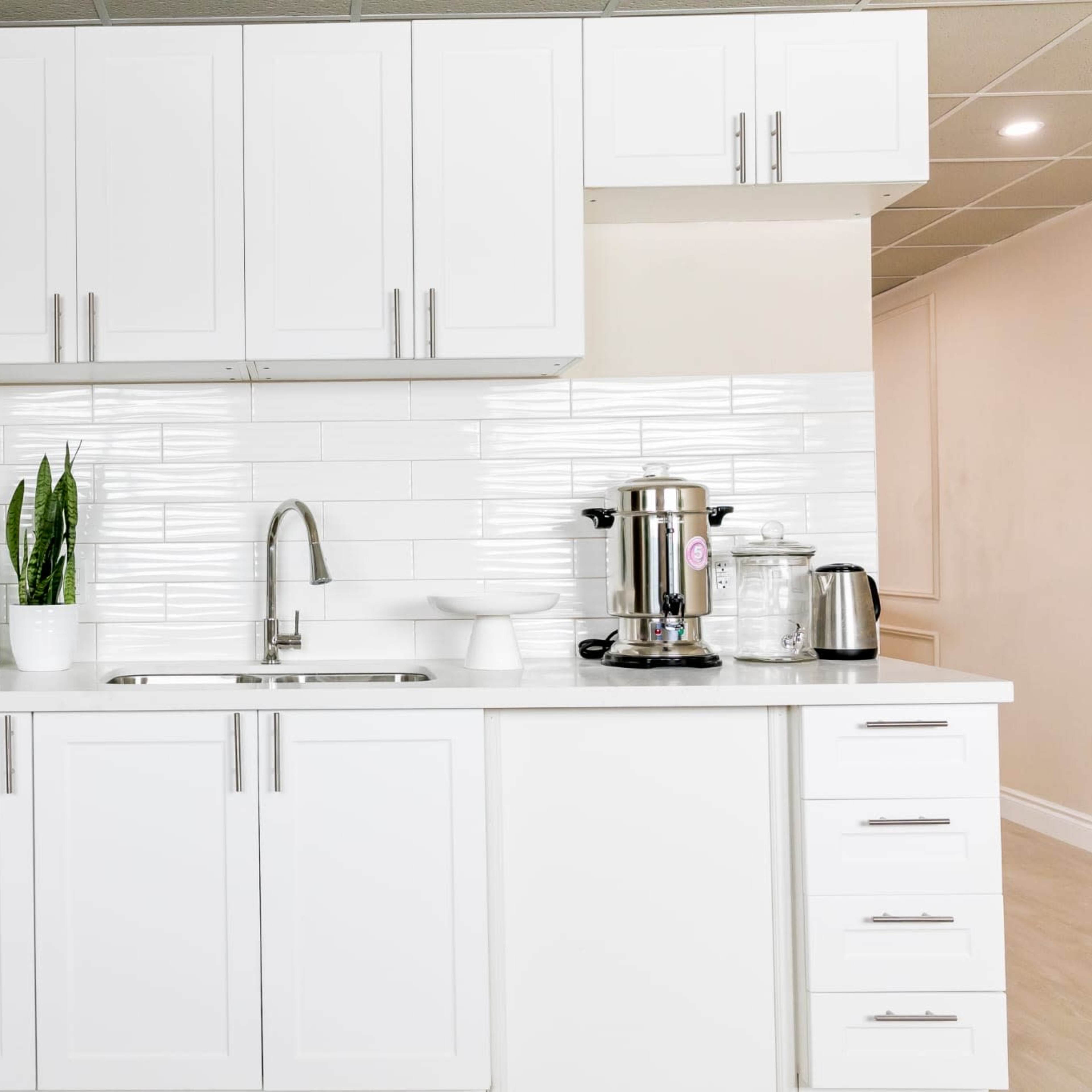 A modern kitchen with white cabinets, a stainless steel sink, and appliances including a refrigerator, coffee maker, and kettle.