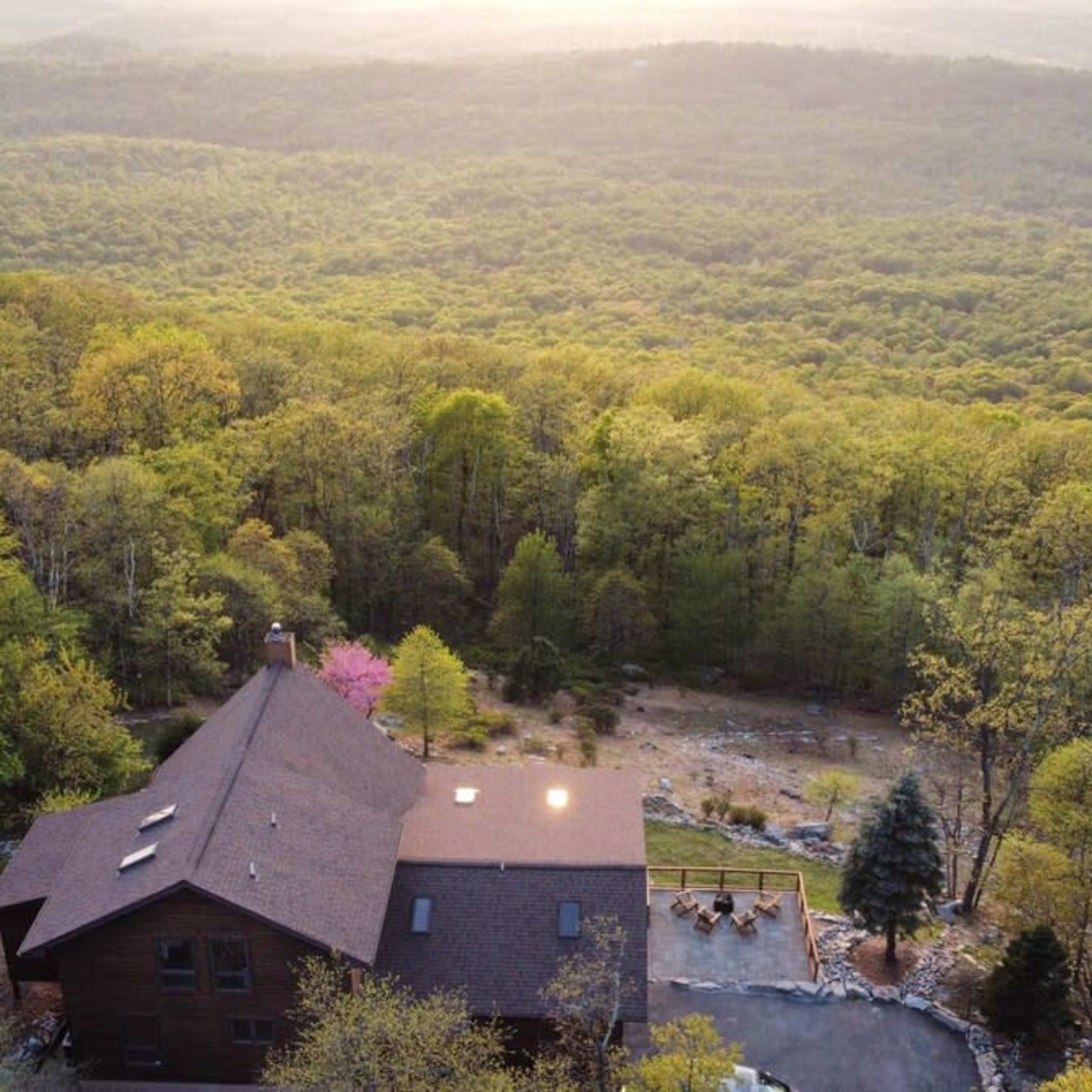 A mountain house is situated on a hillside surrounded by lush green trees and a panoramic view of the valley below.