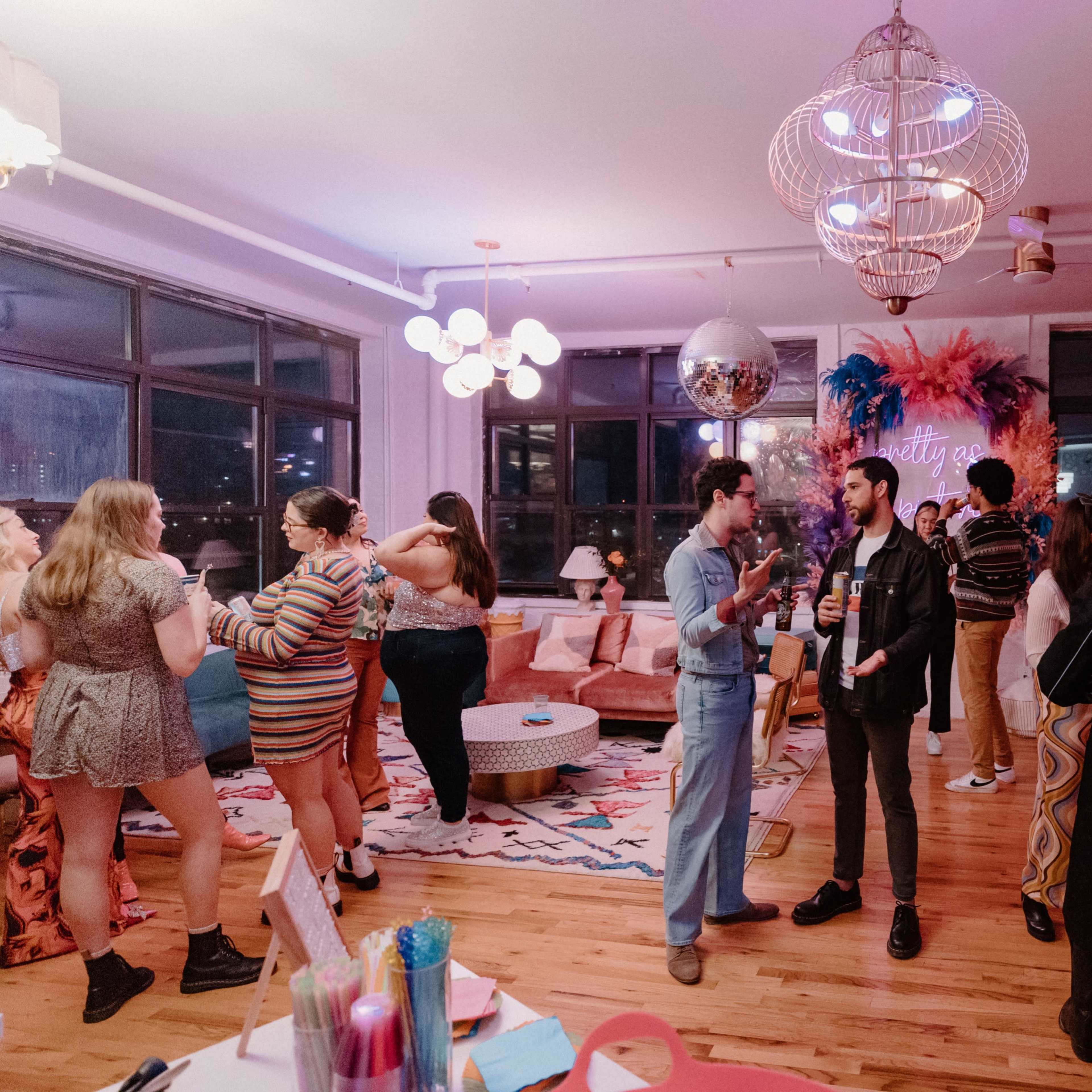 A group of people mingles at a brightly decorated indoor party, surrounded by colorful decor and furniture.