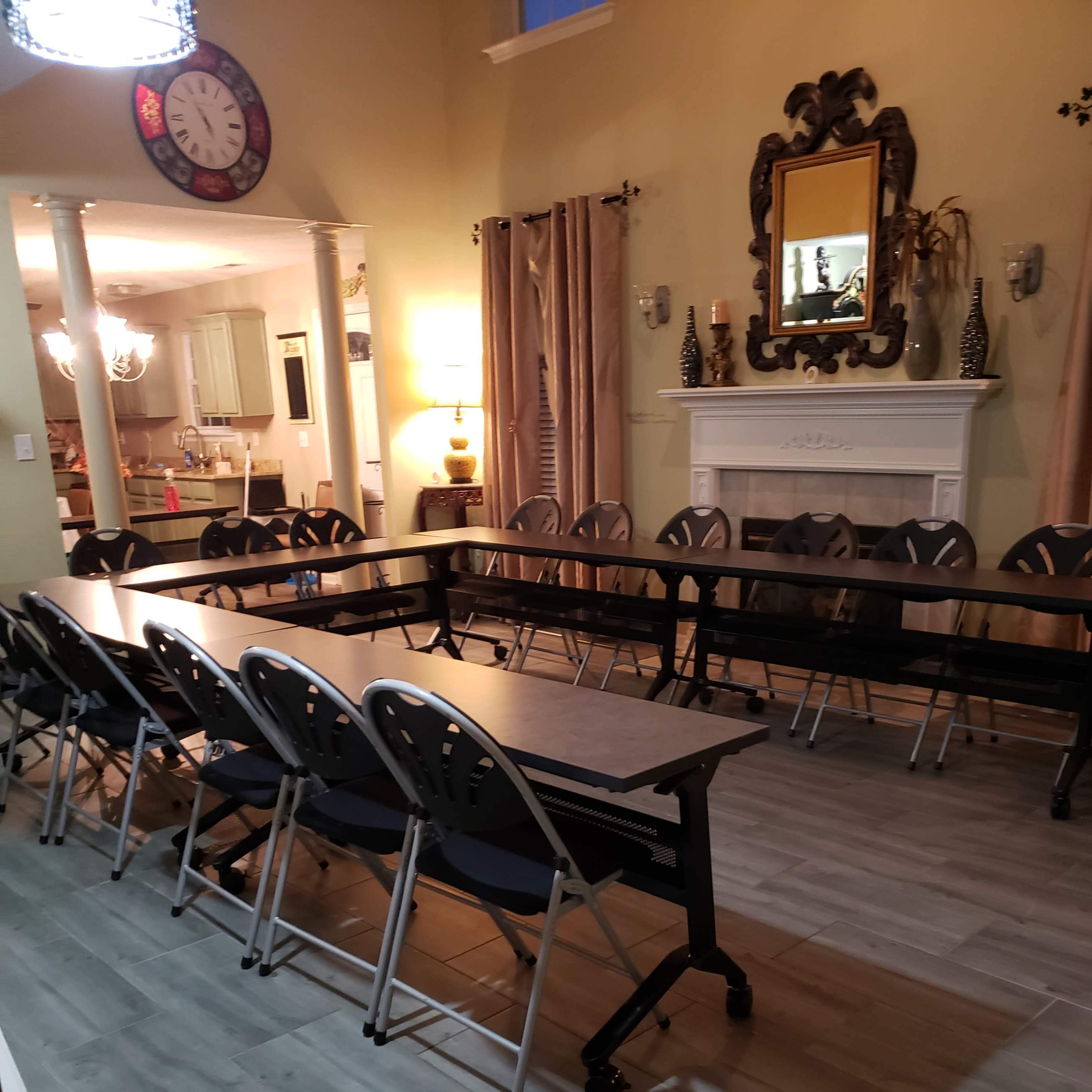 A long table with folding chairs is set up in a spacious room that features a fireplace and decorative wall mirrors.