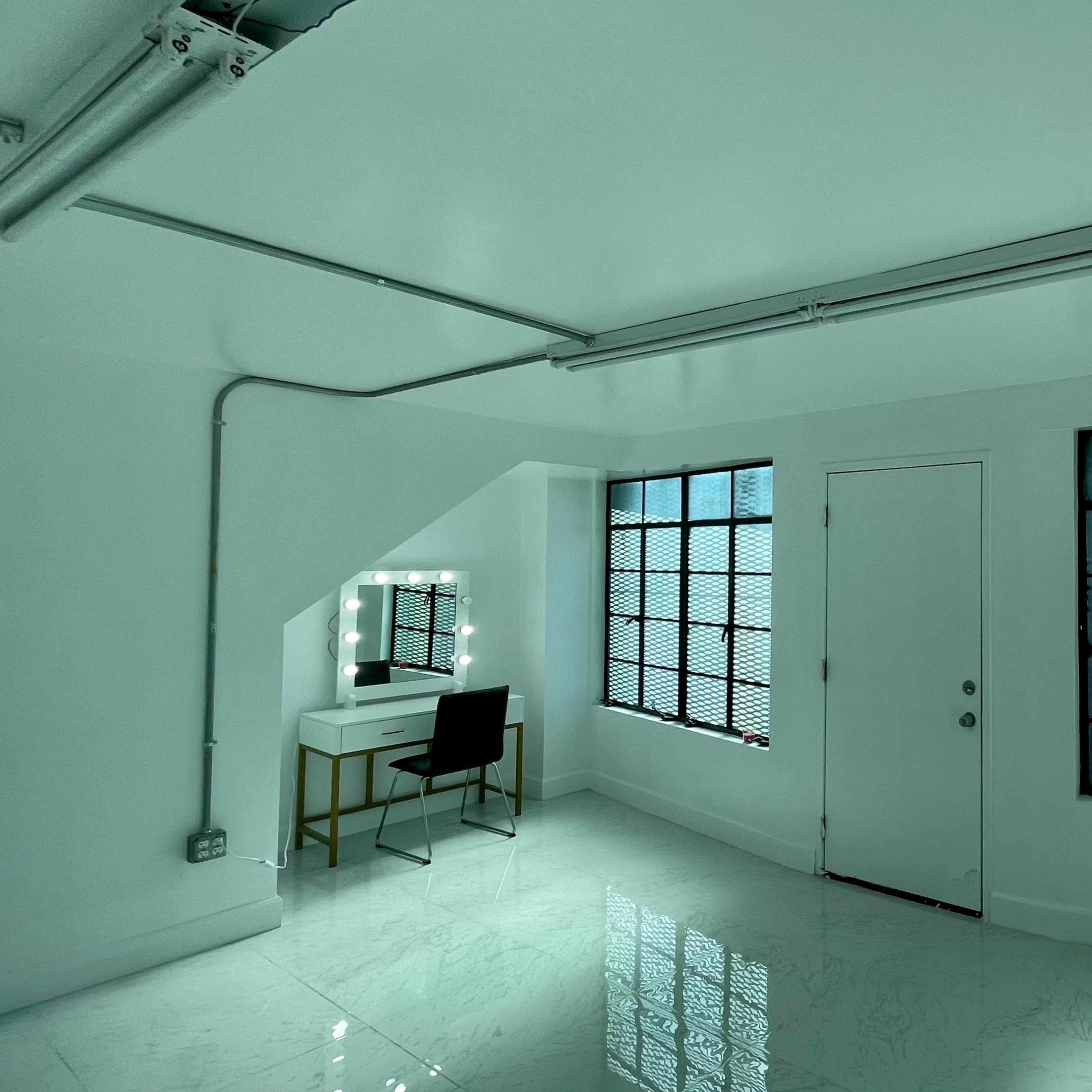 The room features white walls, glossy tile flooring, two large windows with metal grilles, and a vanity table with a chair.