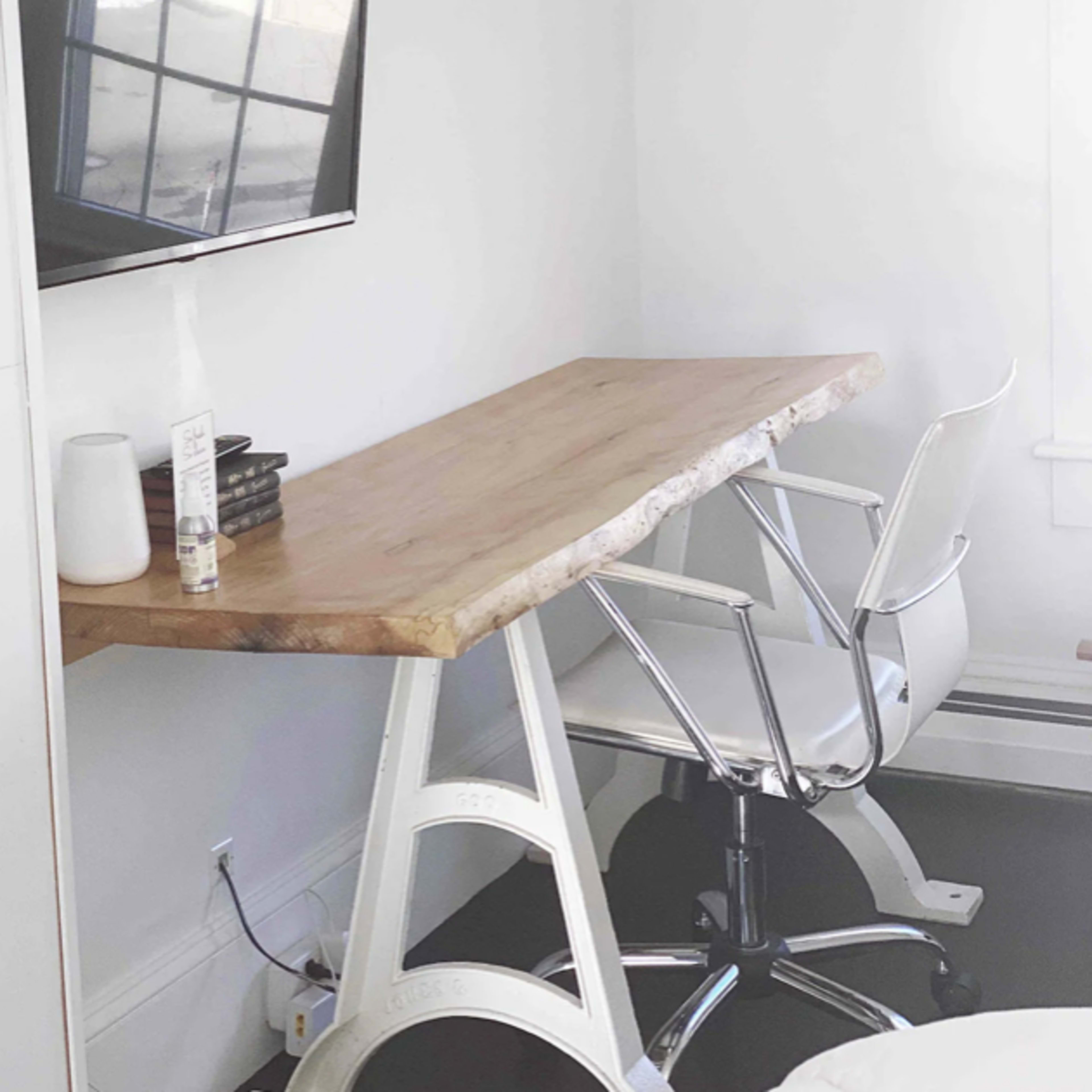 A small workspace features a wooden desk with a metal base, a sleek white chair, and a wall-mounted television.