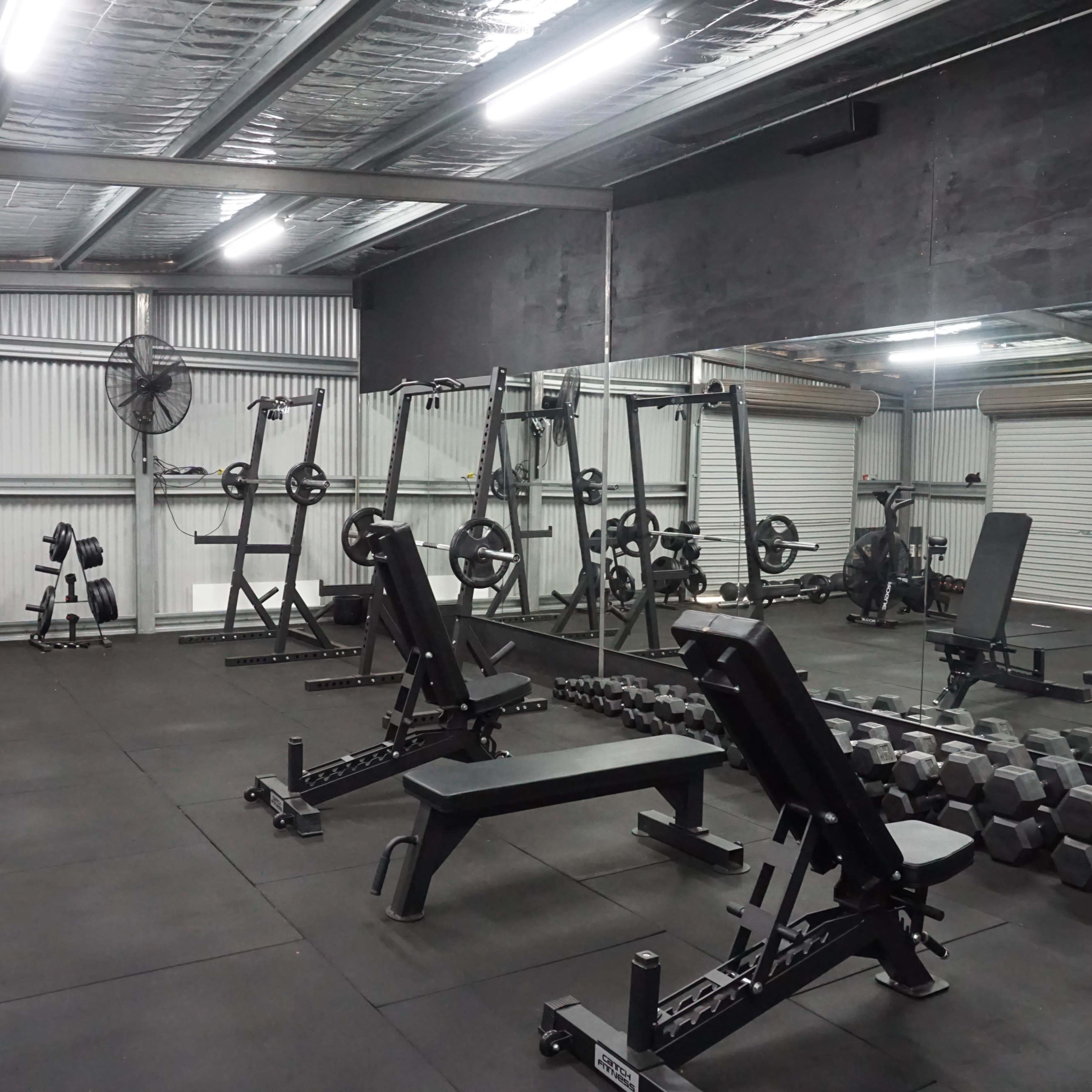 A gym interior with various weightlifting equipment, including benches, dumbbells, and a power rack, set on a rubber flooring.