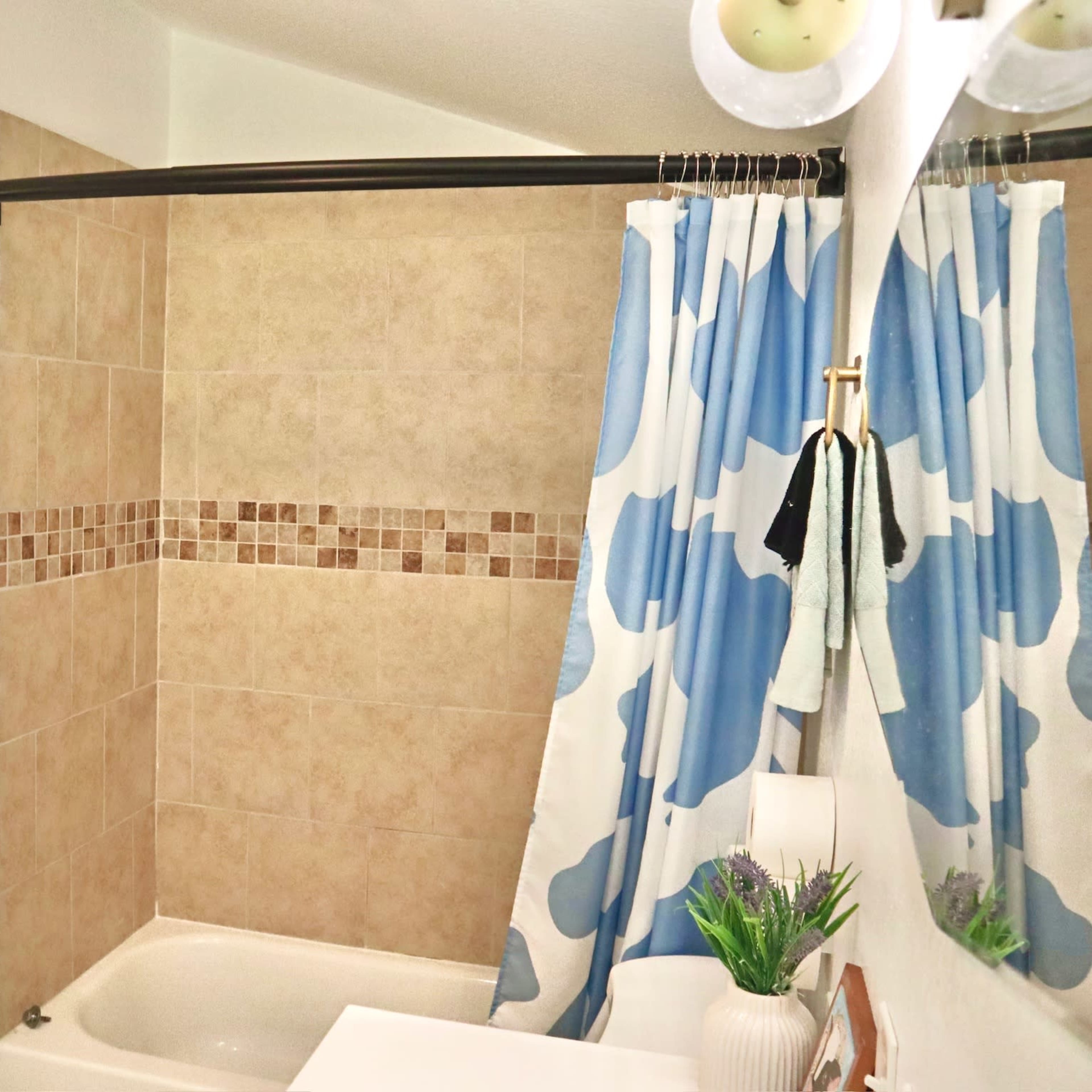 A bathroom features a bathtub with tiled walls, a shower curtain with a blue and white pattern, and a towel hanging on the door.
