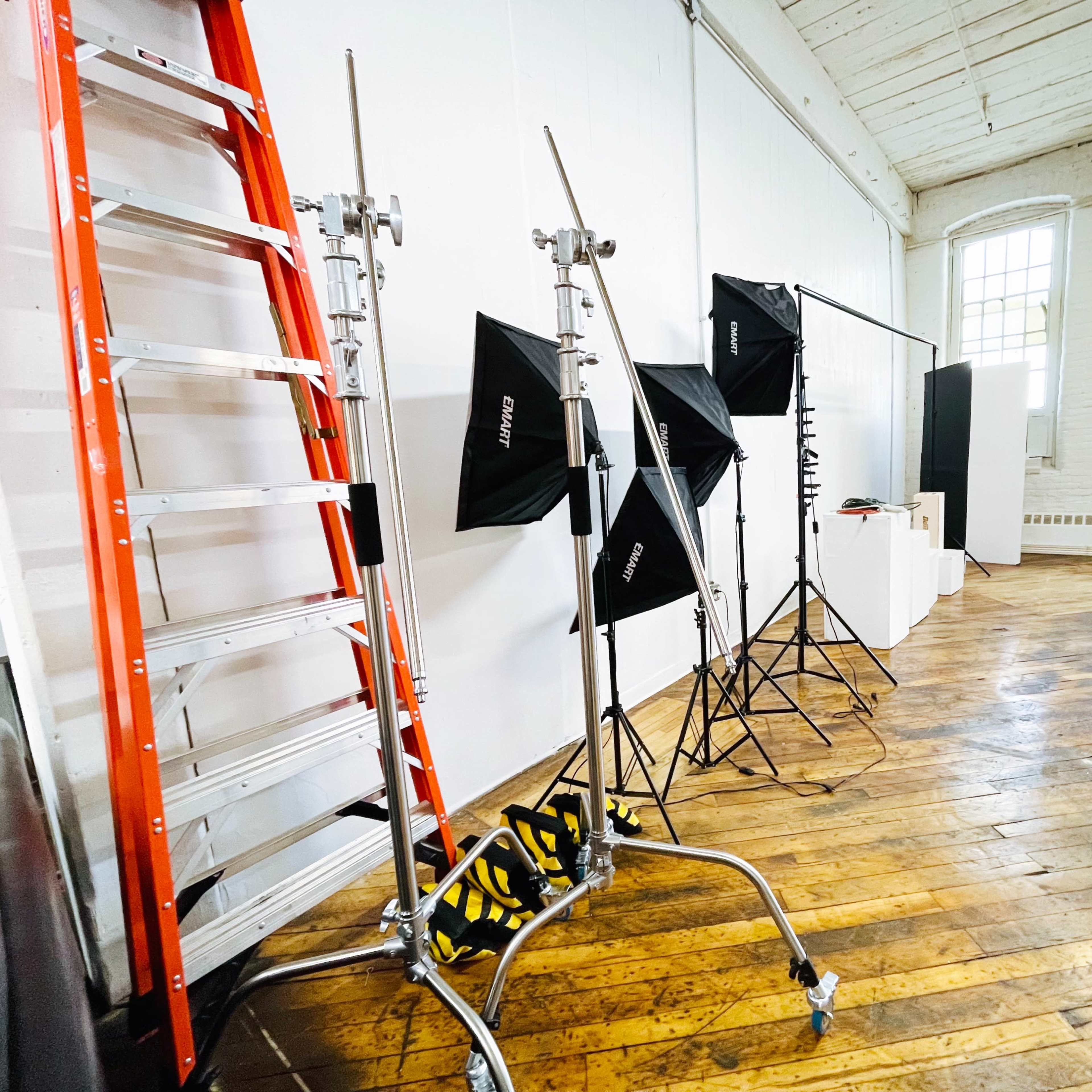 A photography studio with a wooden floor, a ladder, light stands, and lighting equipment.