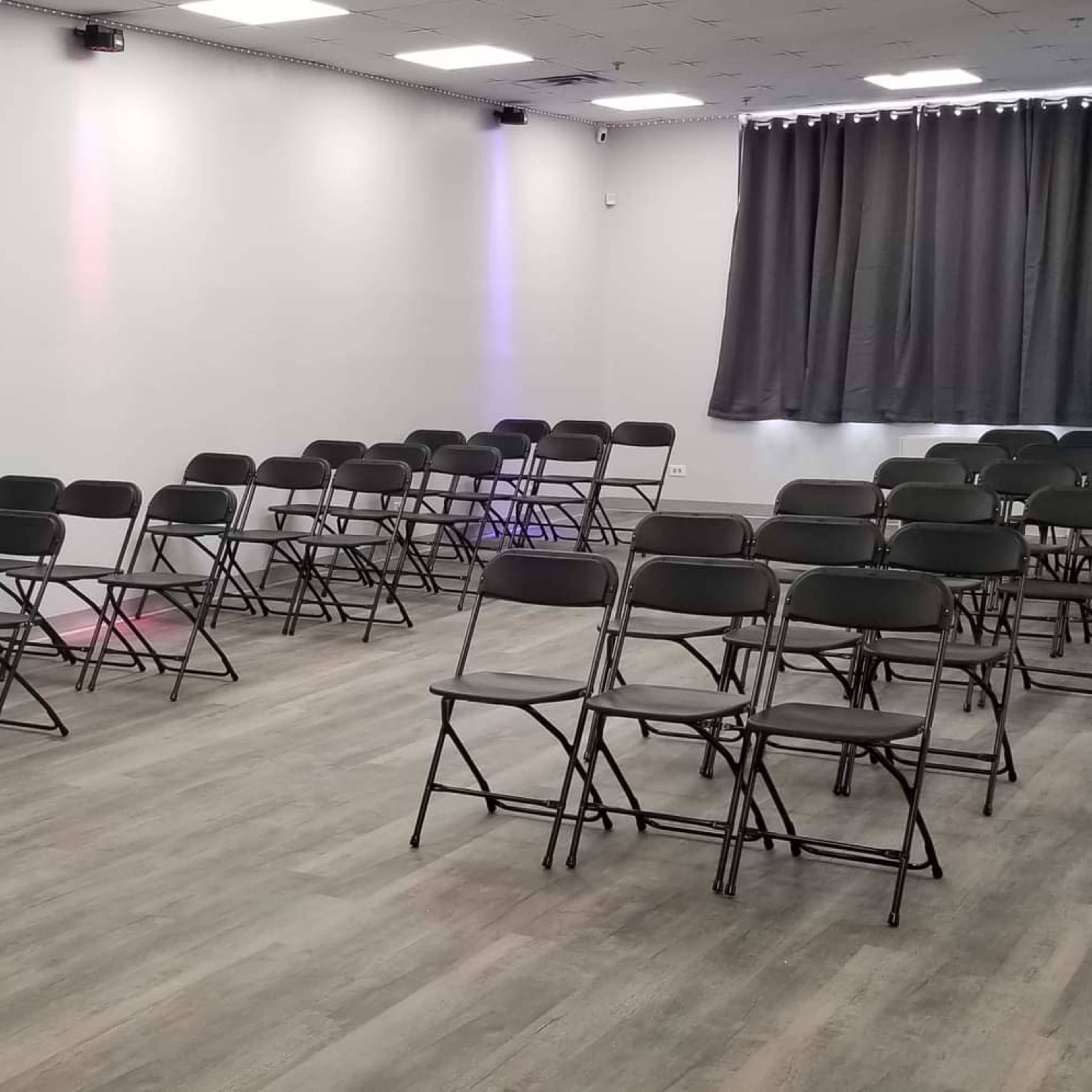 A room set up with rows of black folding chairs and a tall round table in the front.
