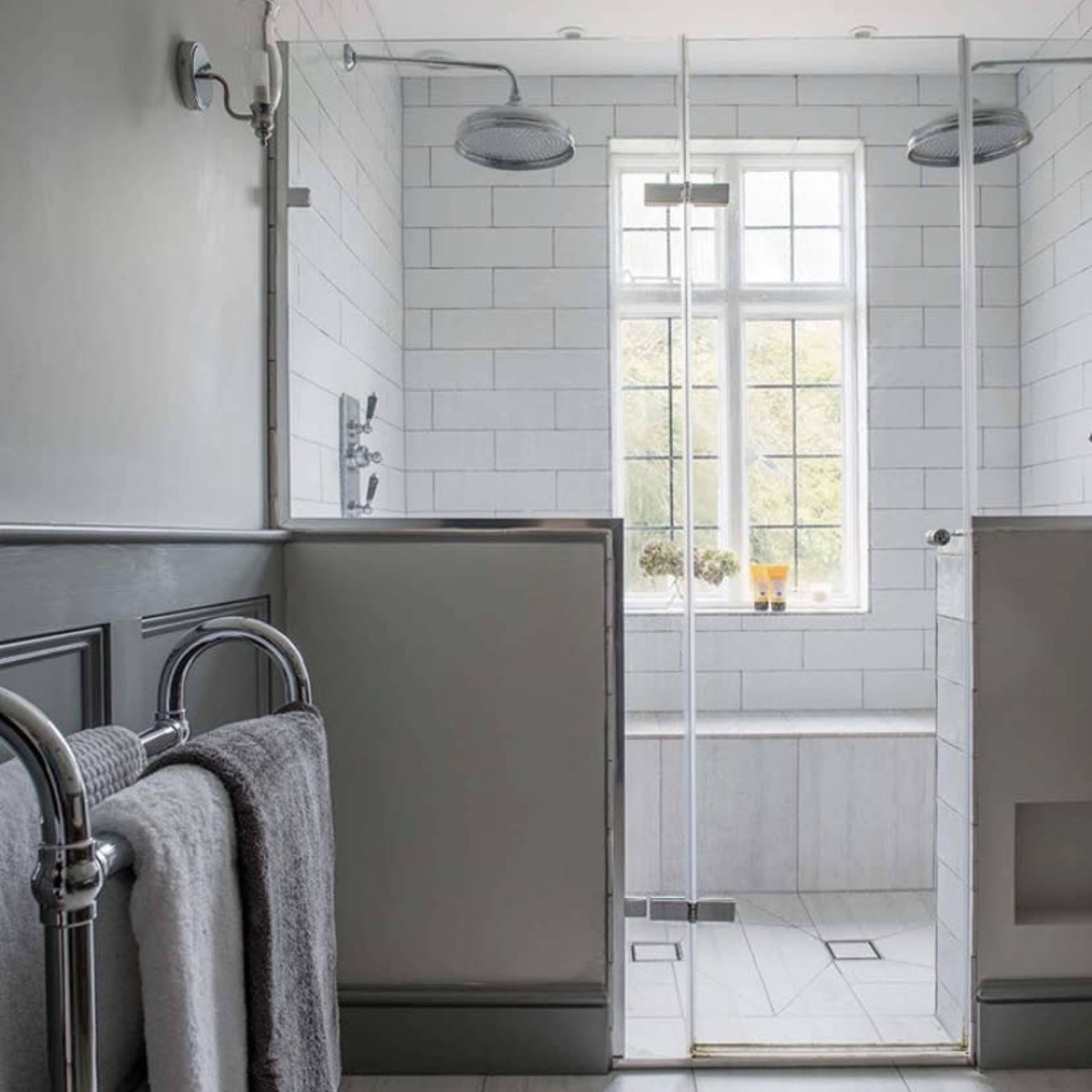 A modern bathroom with a glass shower enclosure, white tiled walls, and natural light coming through a window.