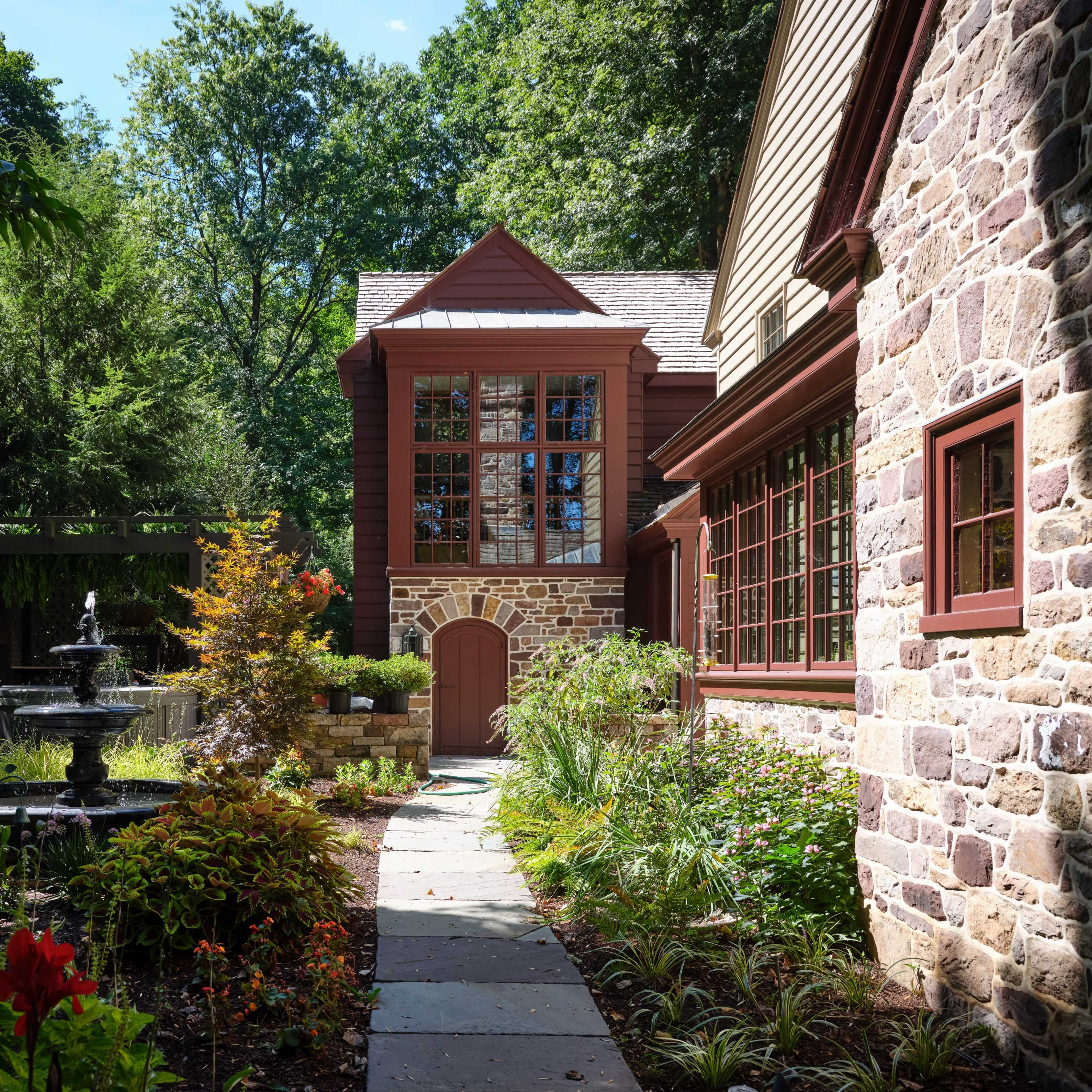 A landscaped pathway leading to a stone building with large windows, flanked by greenery and a fountain.