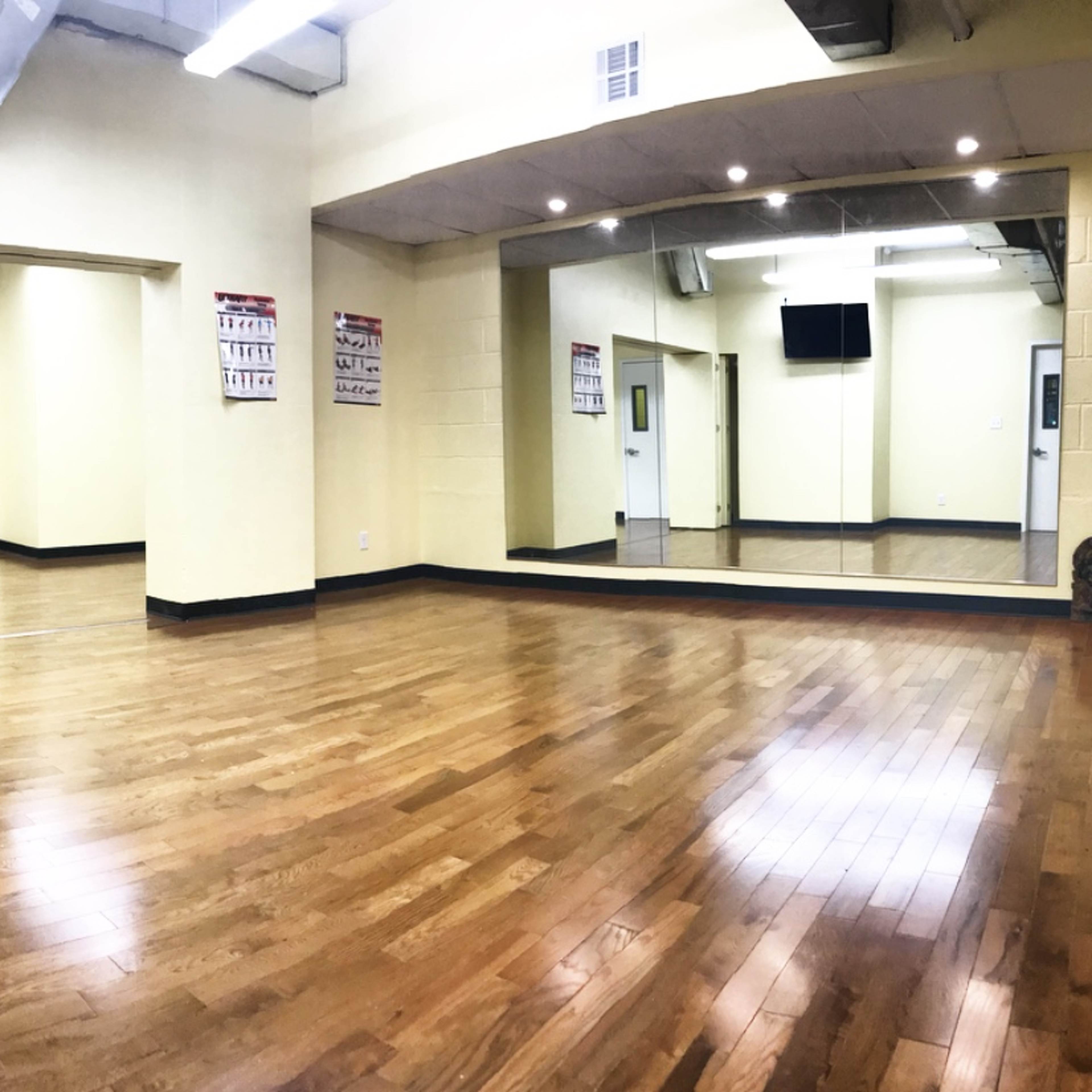 A spacious room with polished wooden floors, yellow walls, and a large mirror on one side.