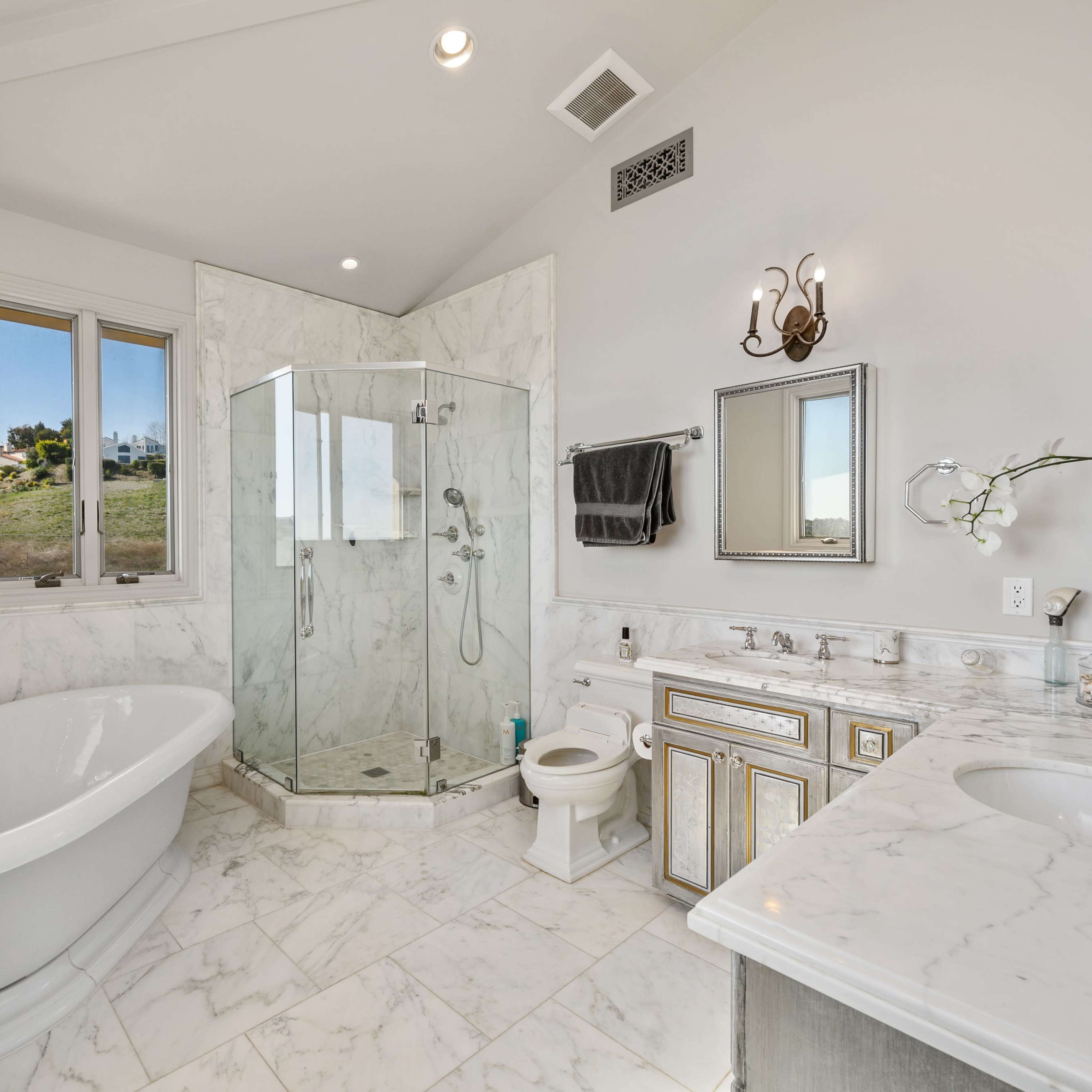 A spacious bathroom featuring a freestanding bathtub, a glass-enclosed shower, and dual sinks with marble countertops.