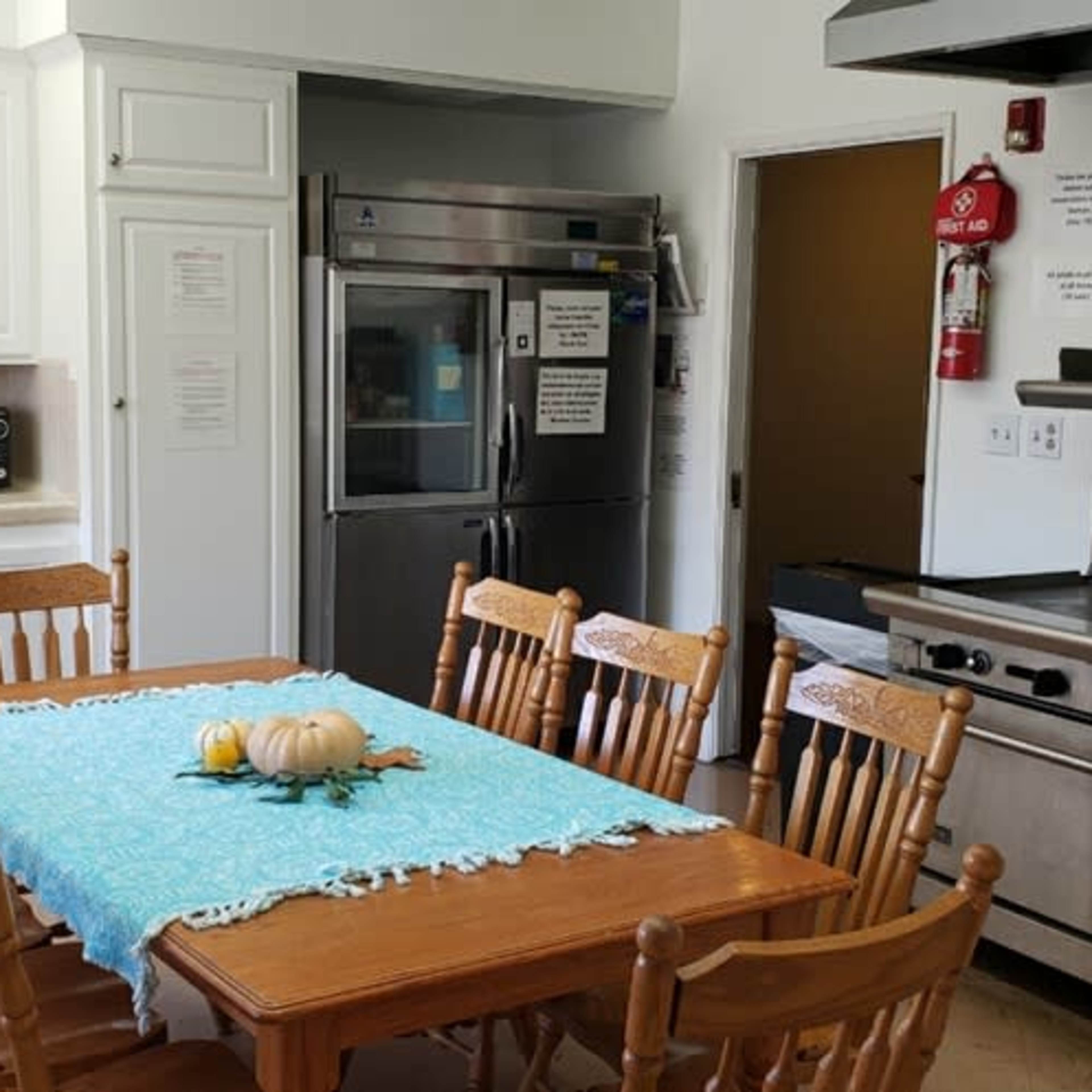 A bright kitchen with a wooden dining table surrounded by chairs, a large refrigerator, and a commercial-grade stove.