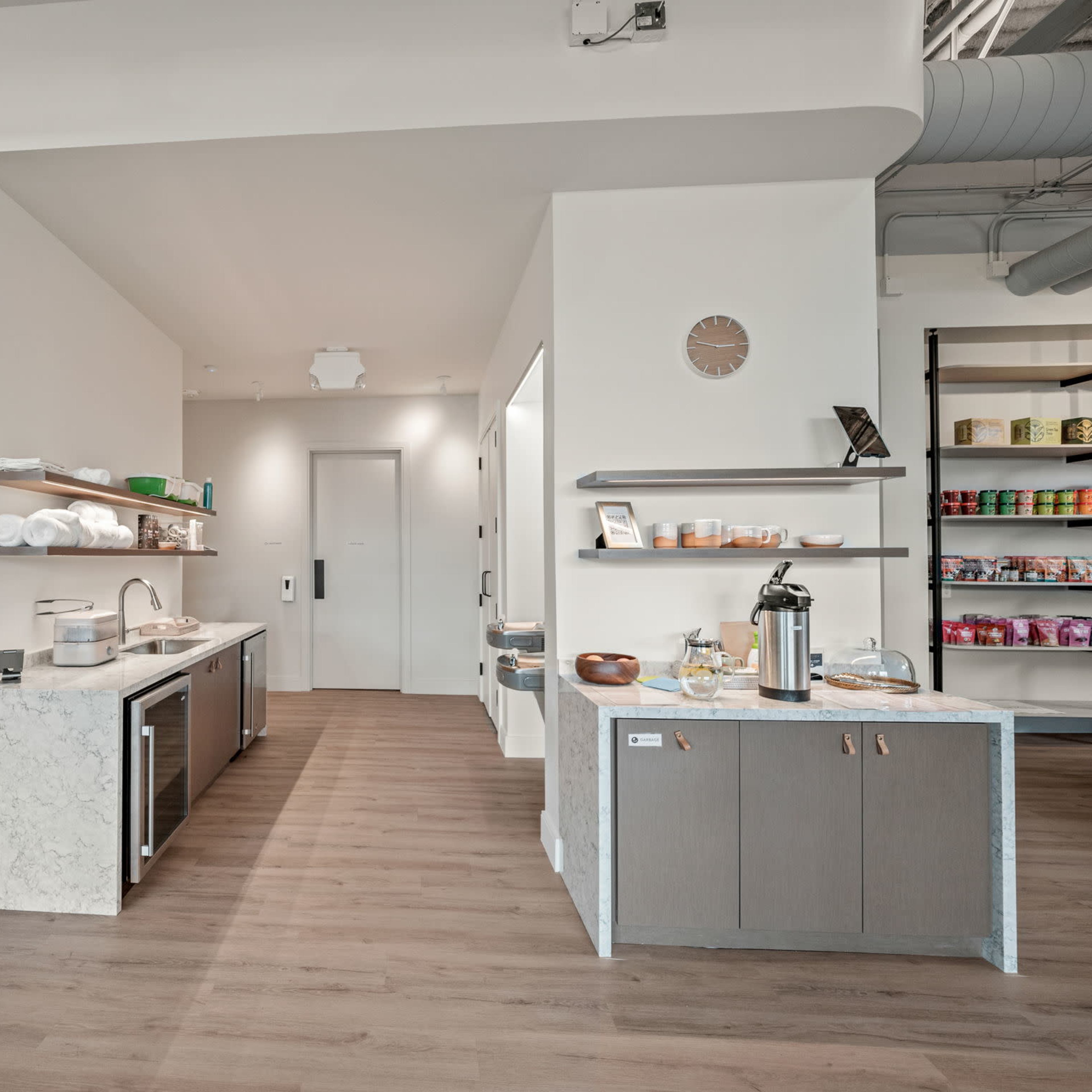 A modern interior features a kitchen area with a marble countertop and organized shelves displaying storage containers and products.