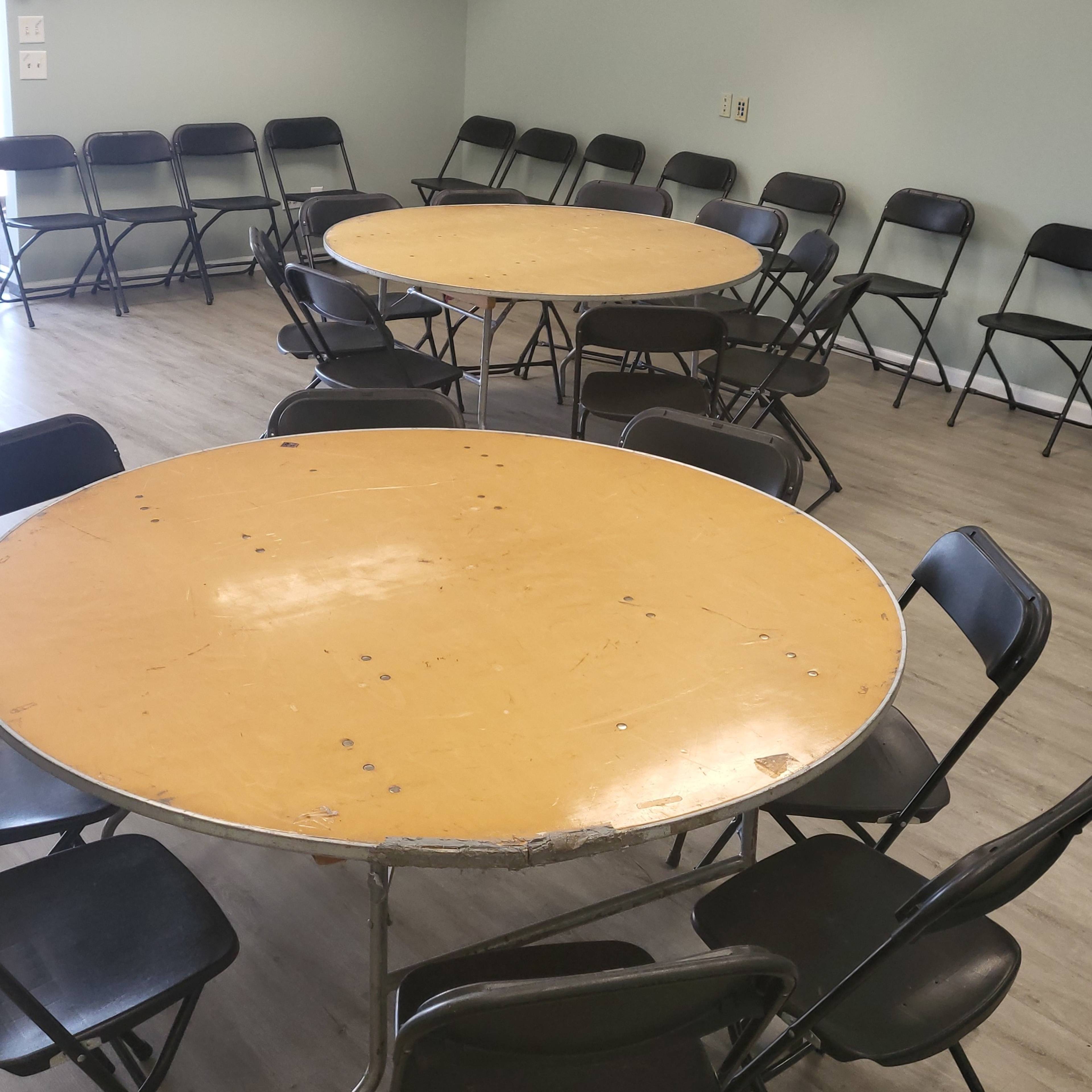 A meeting room with two round tables surrounded by black folding chairs arranged in a circle on a wooden floor.
