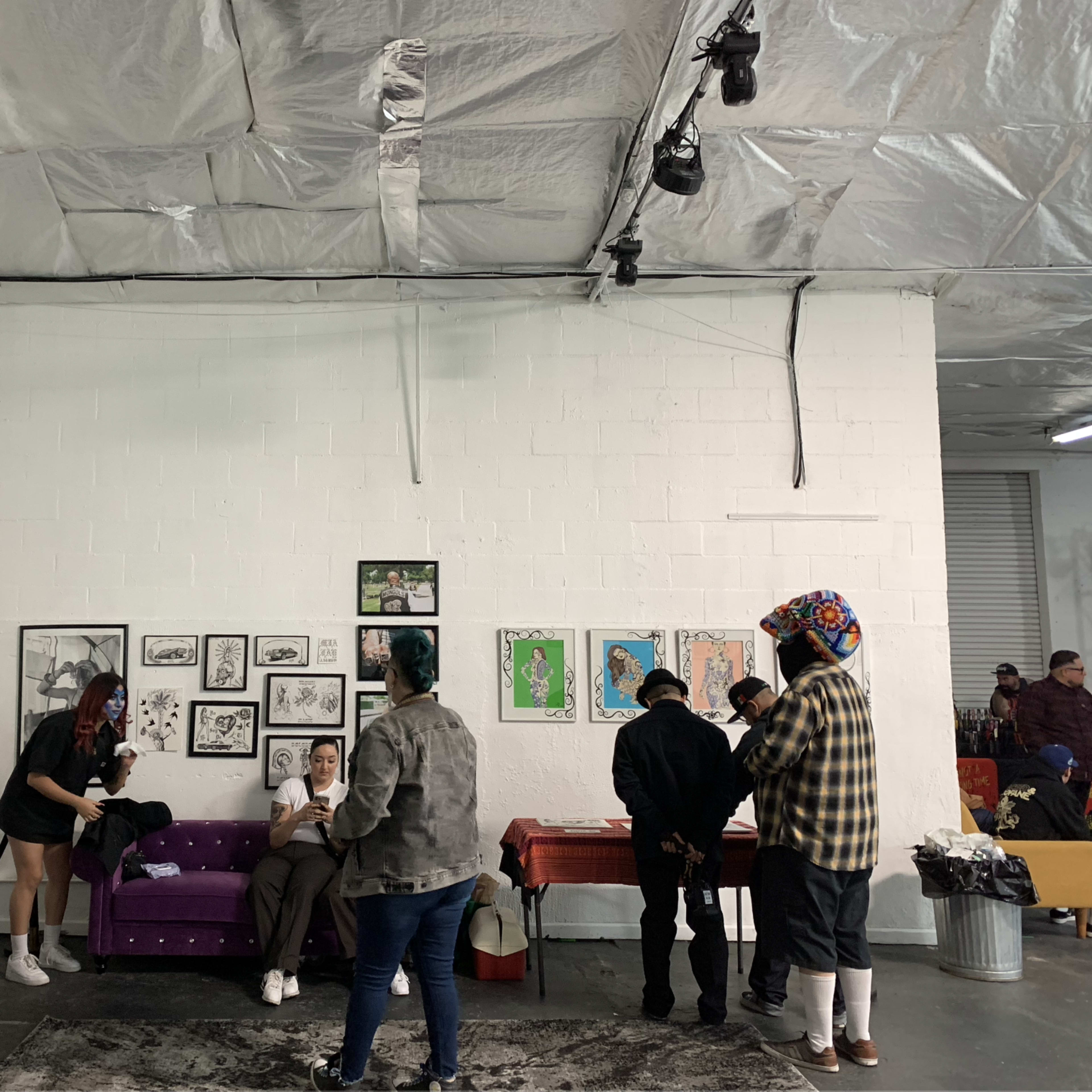 A group of people interacts in a spacious room with artwork displayed on the walls and a purple sofa in the center.