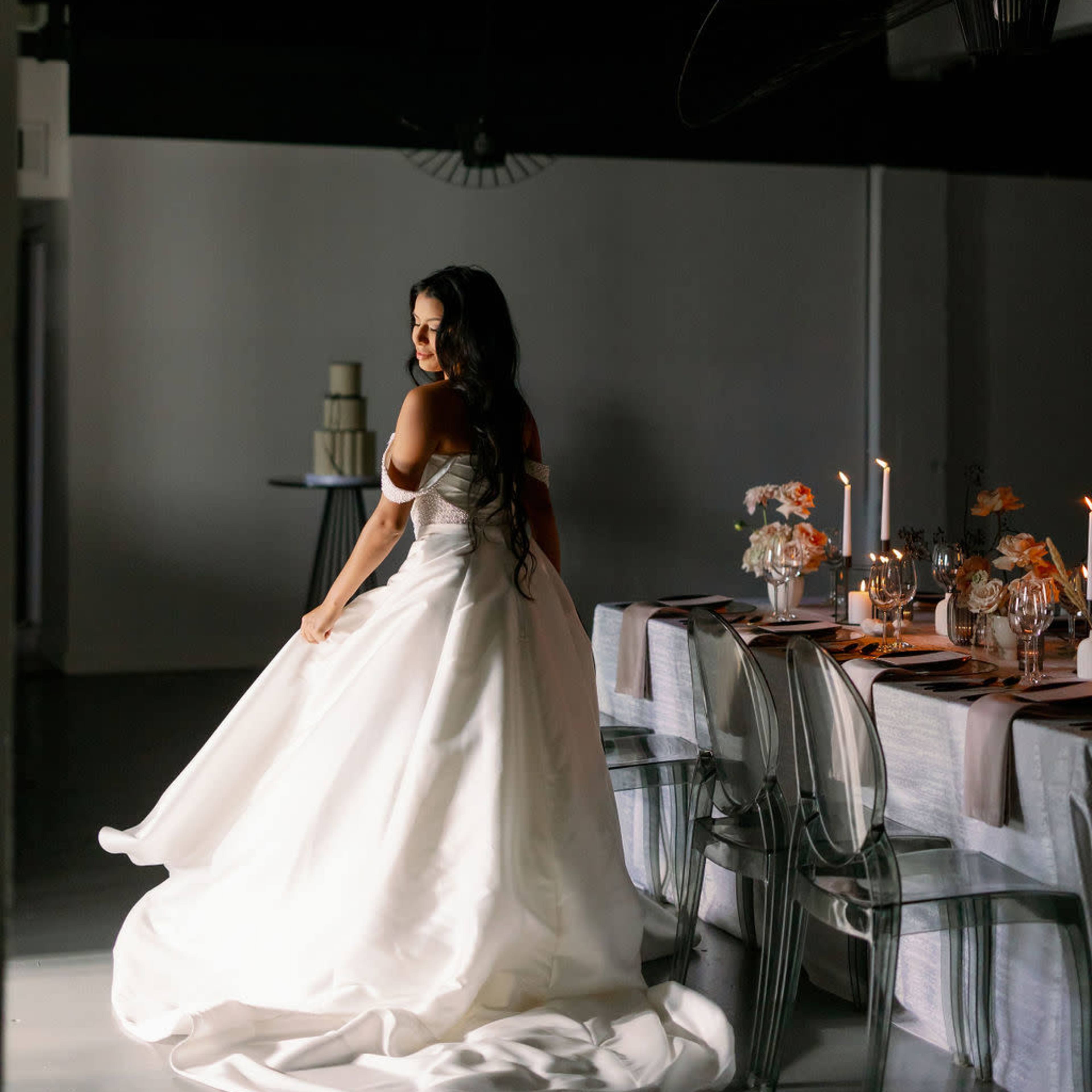 A woman in a wedding gown twirls in a dimly lit dining space adorned with a table set for a formal meal.