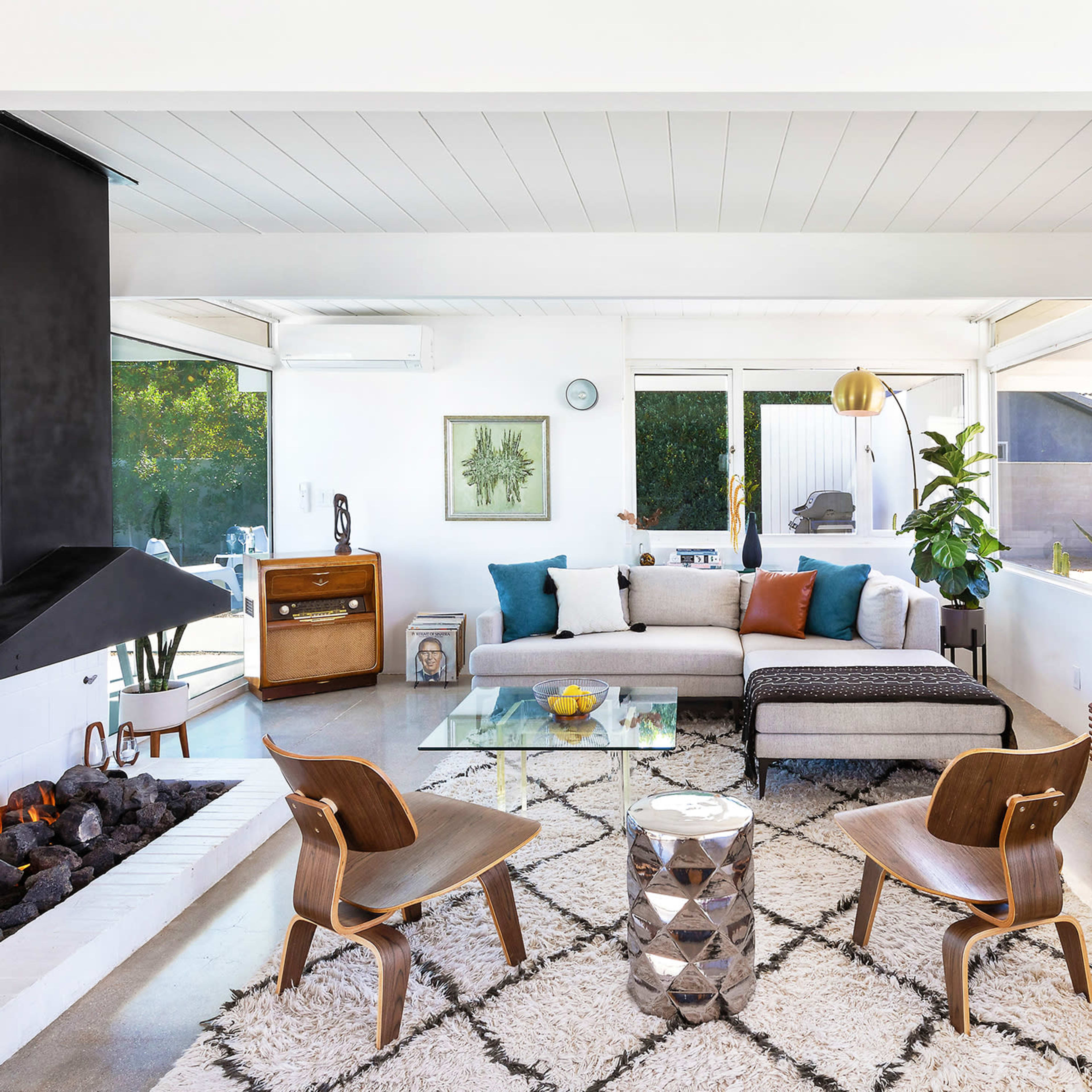 A modern living room with a sectional sofa, two wooden chairs, a glass coffee table, and a black fireplace.