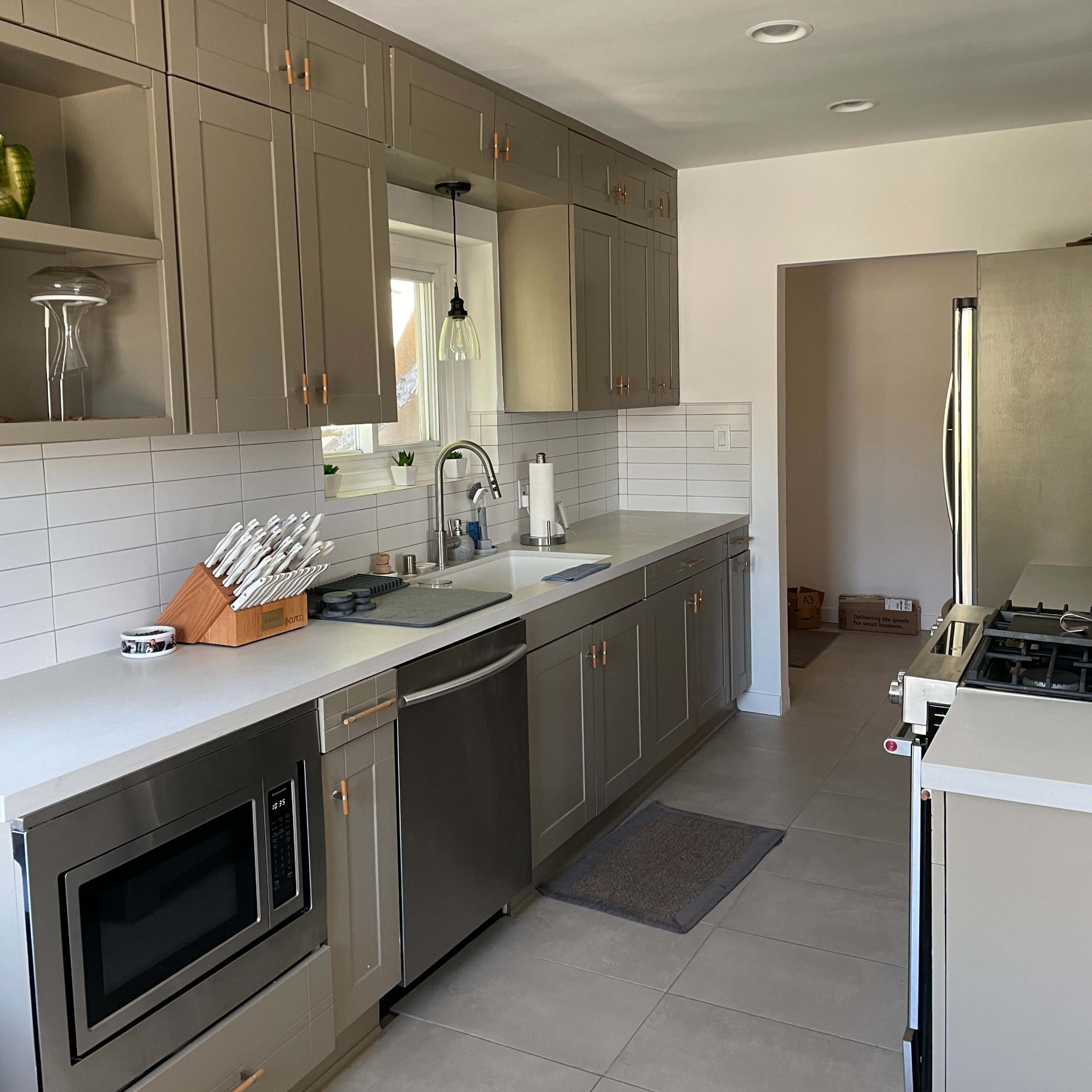 A modern kitchen features gray cabinets, a stainless steel sink, and stainless appliances, with a window providing natural light.