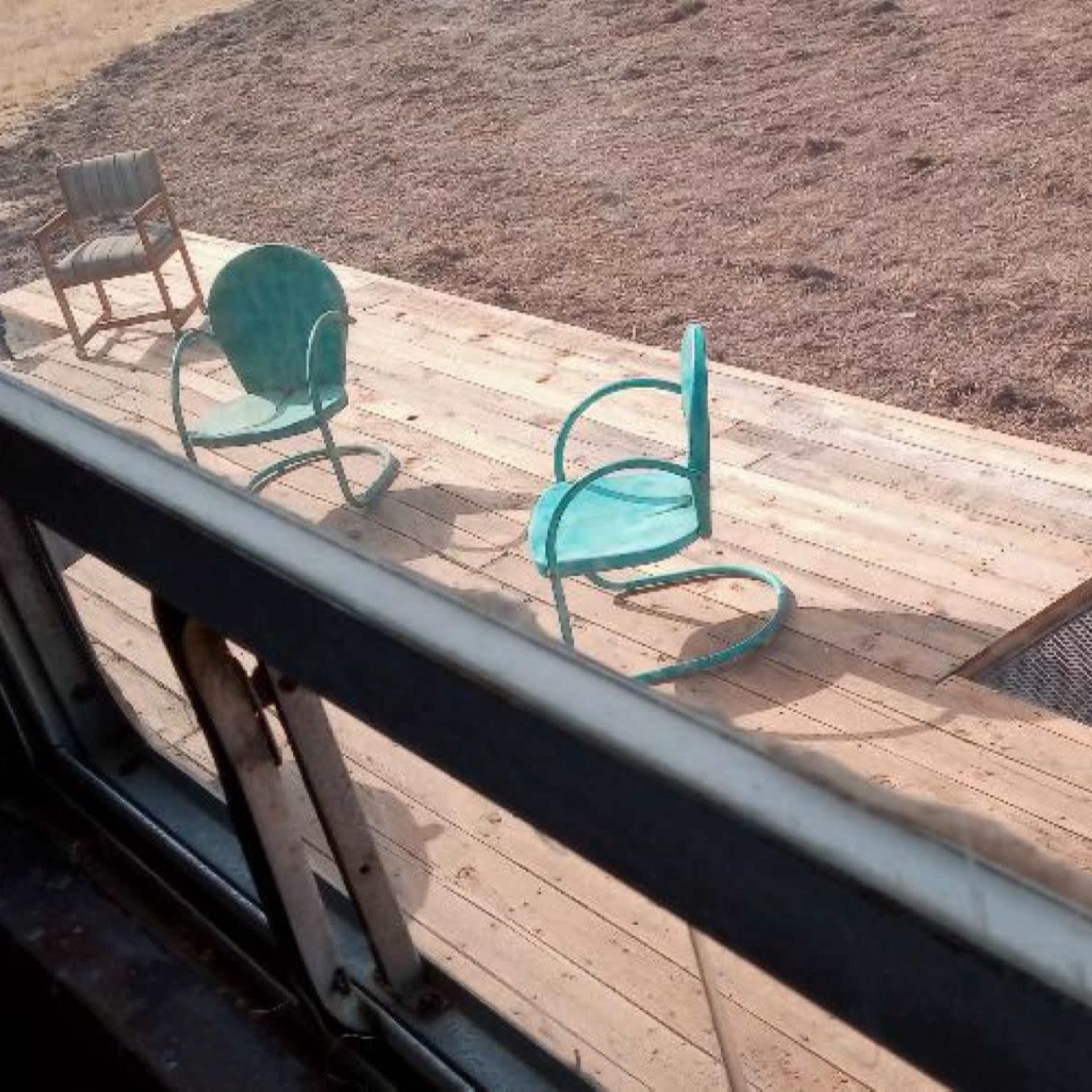 A wooden deck with two chairs and a set of metal stairs leading down to a bare, dry yard.