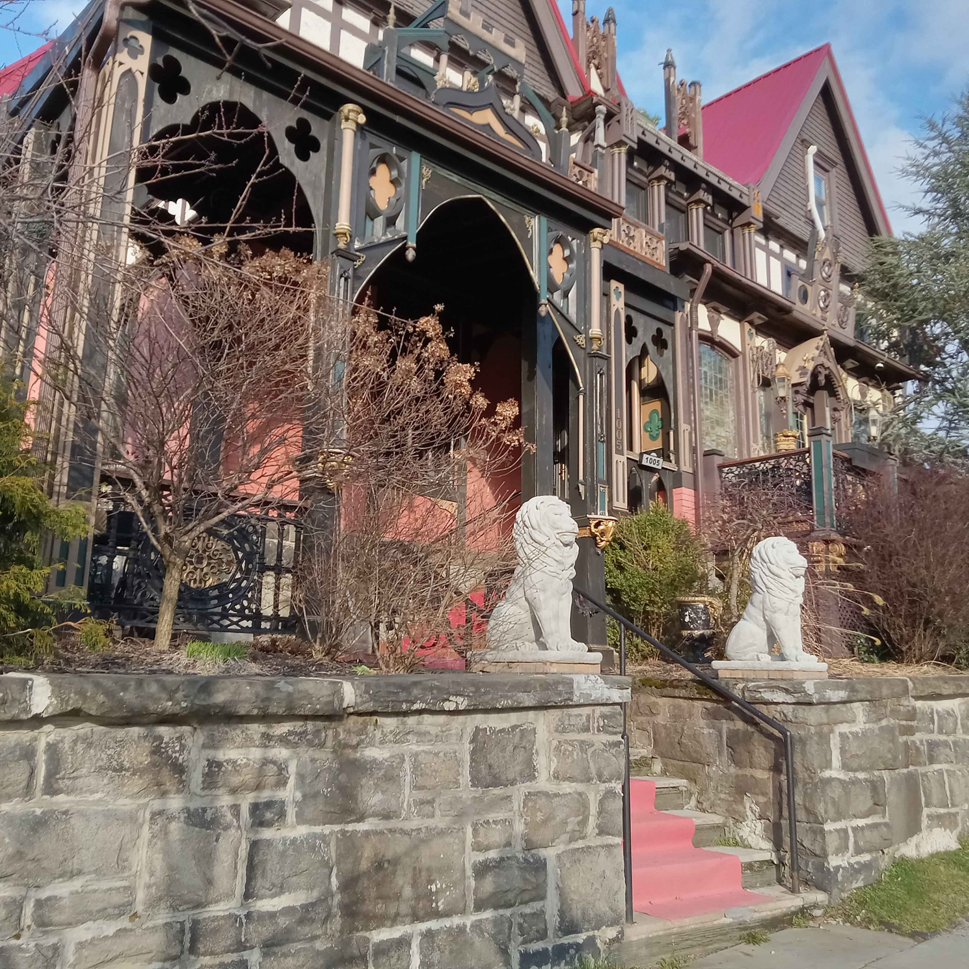 A large Victorian-style house with ornate architecture, featuring a red roof and stone lion statues flanking its entrance.