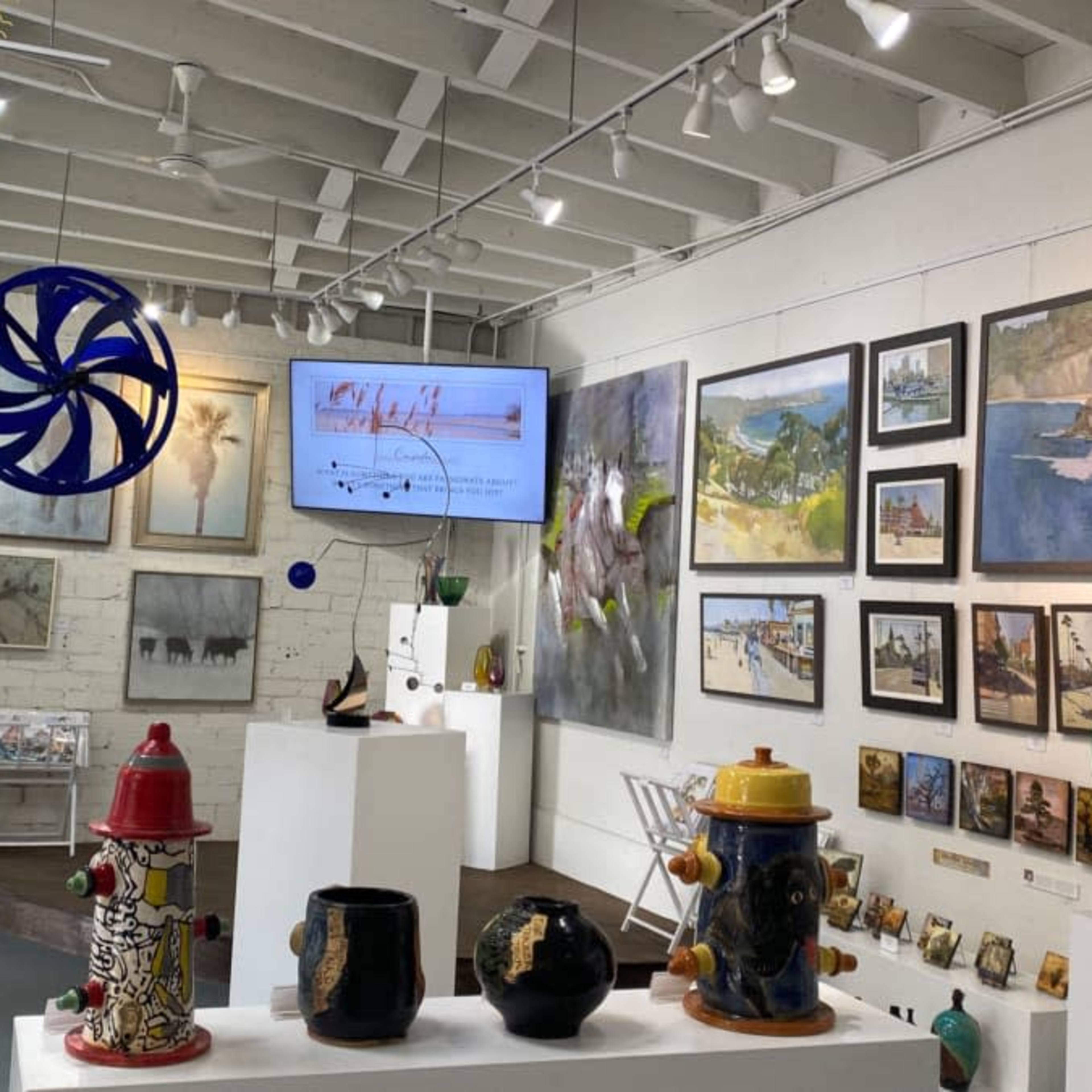 An art gallery featuring various artworks on the walls, displayed sculptures on pedestals, and a large screen showcasing additional visuals.