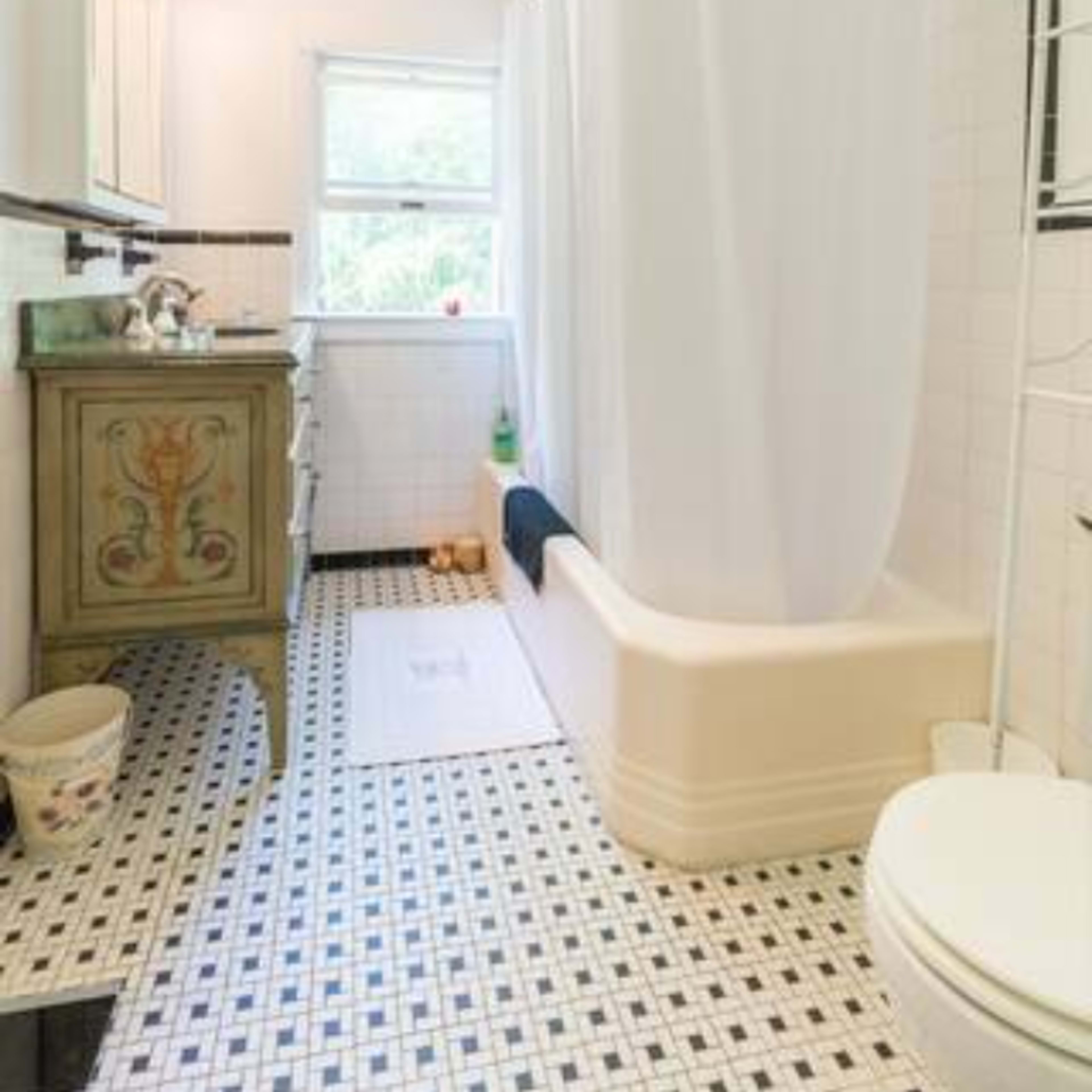 A bathroom with a bathtub covered by a white shower curtain, a wooden cabinet, and black-and-white tiled flooring.
