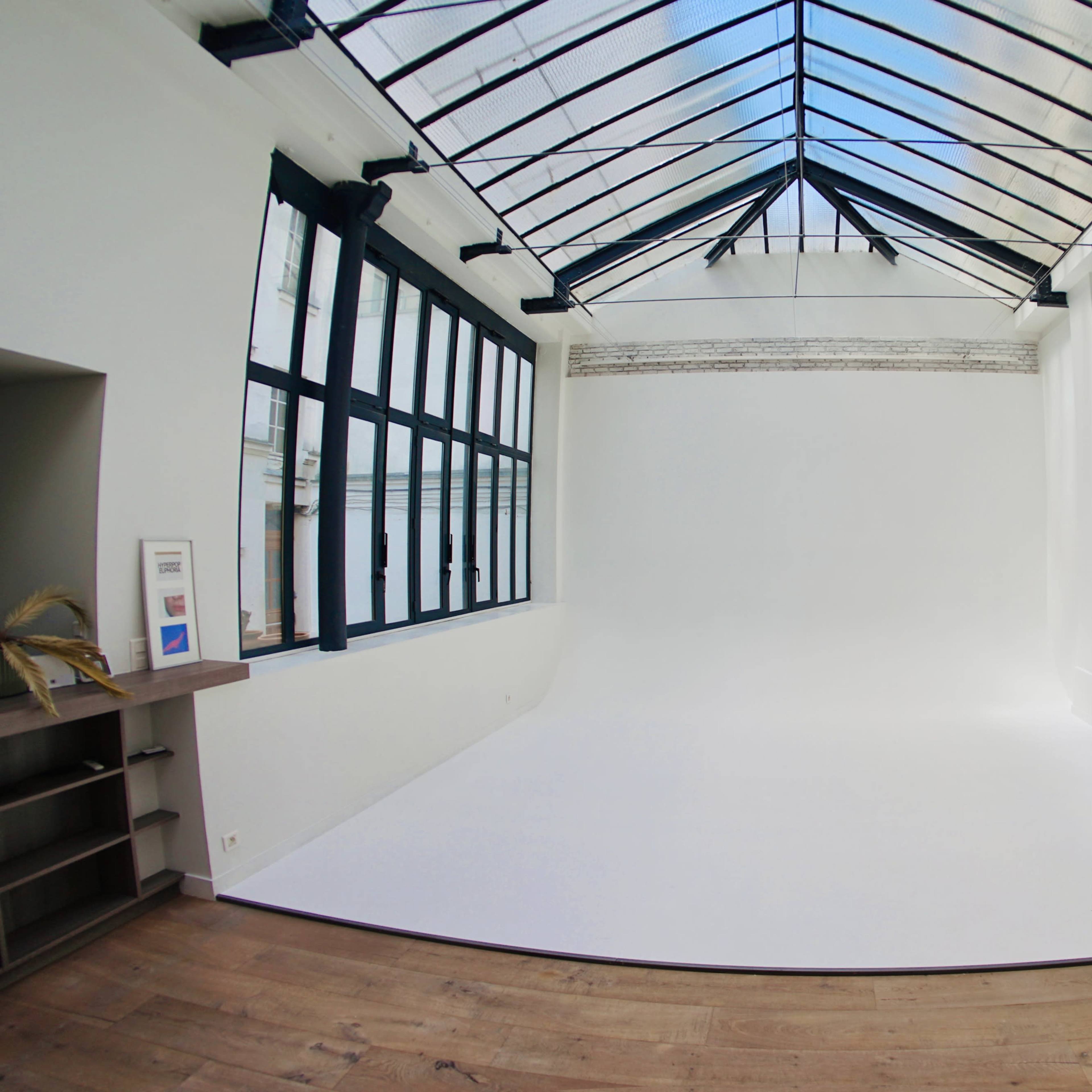 A spacious, well-lit studio featuring a white backdrop and large windows under a glass roof.