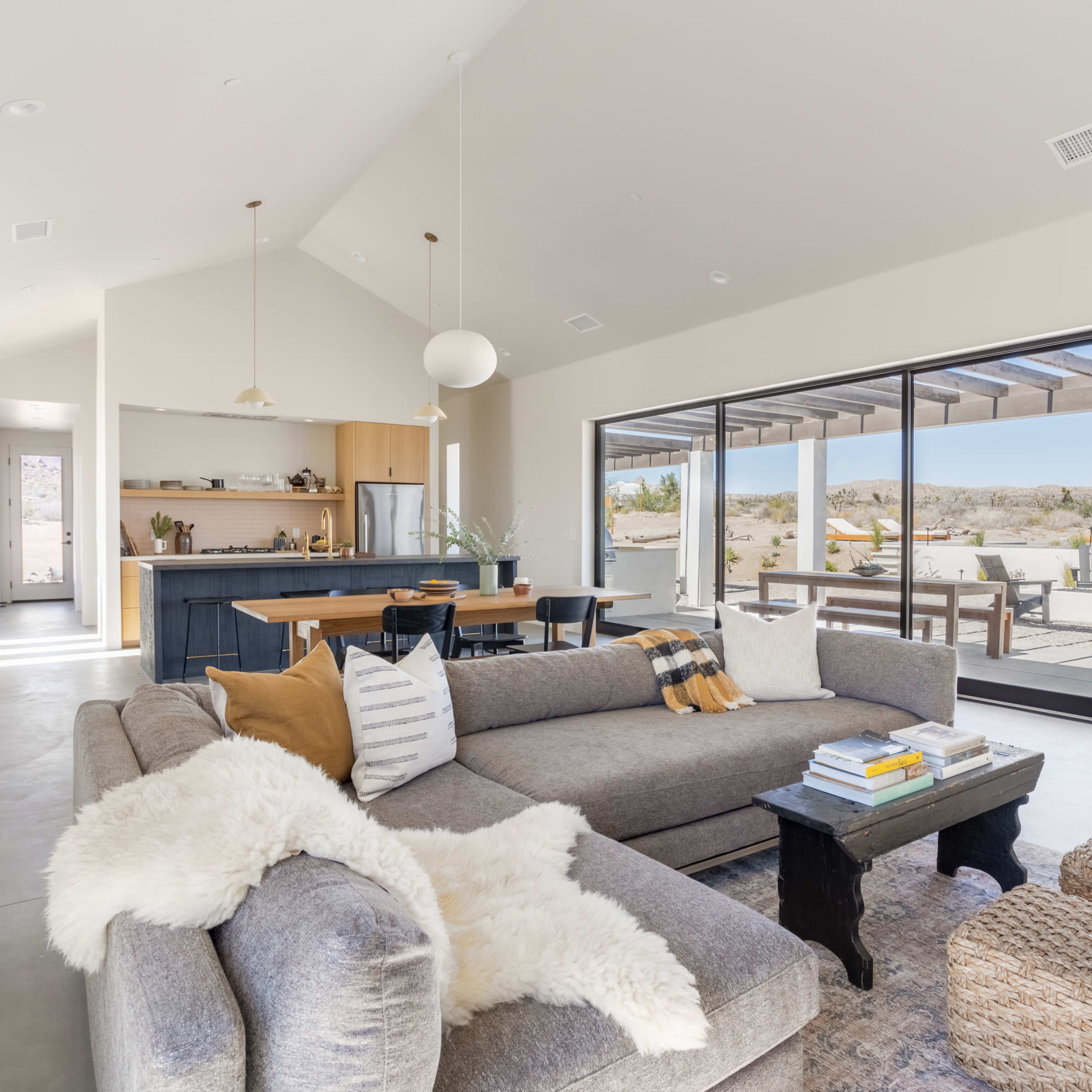 A modern living room with a gray sectional sofa, a coffee table, and a view of an outdoor patio through large glass doors.