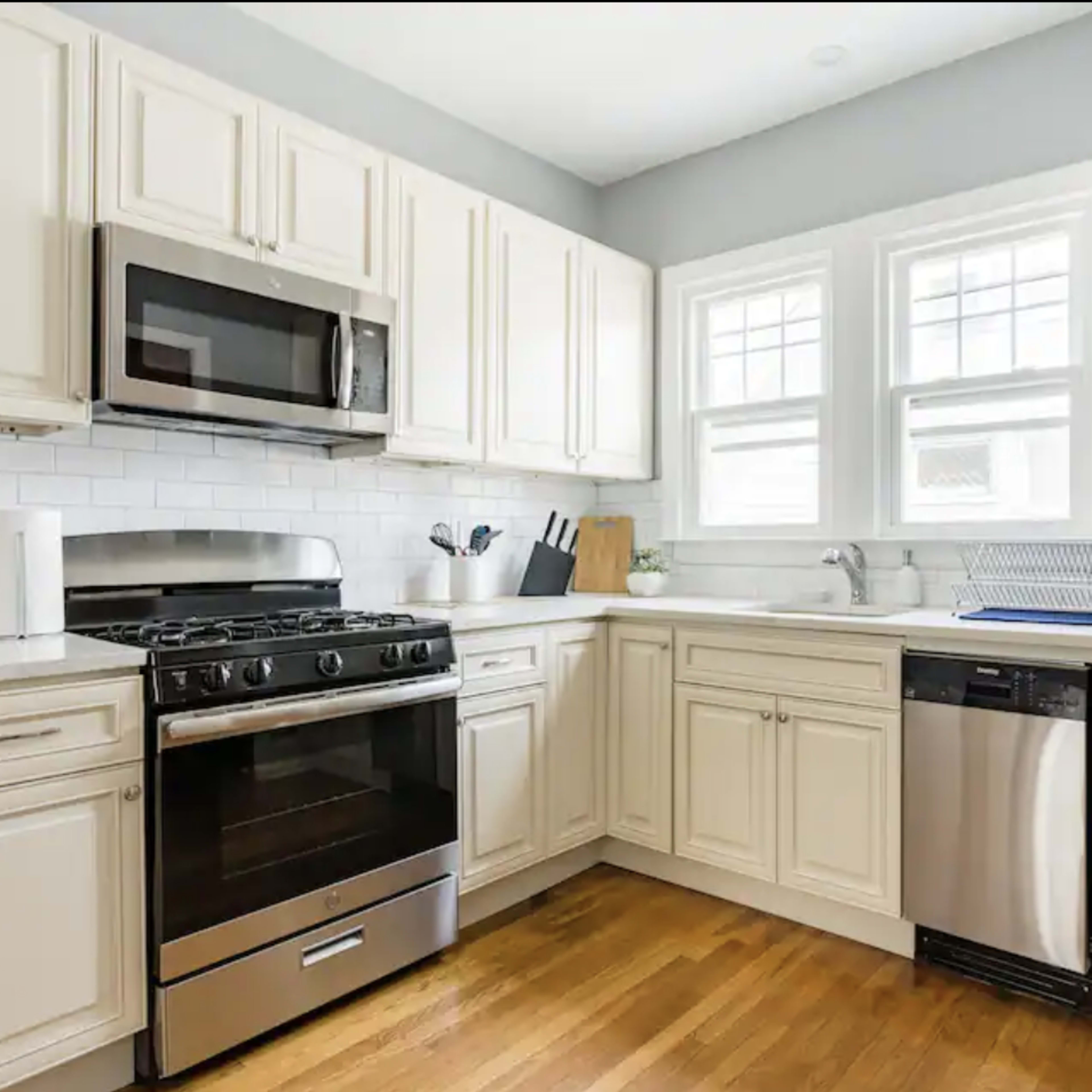 A modern kitchen features white cabinetry, stainless steel appliances, and a hardwood floor.