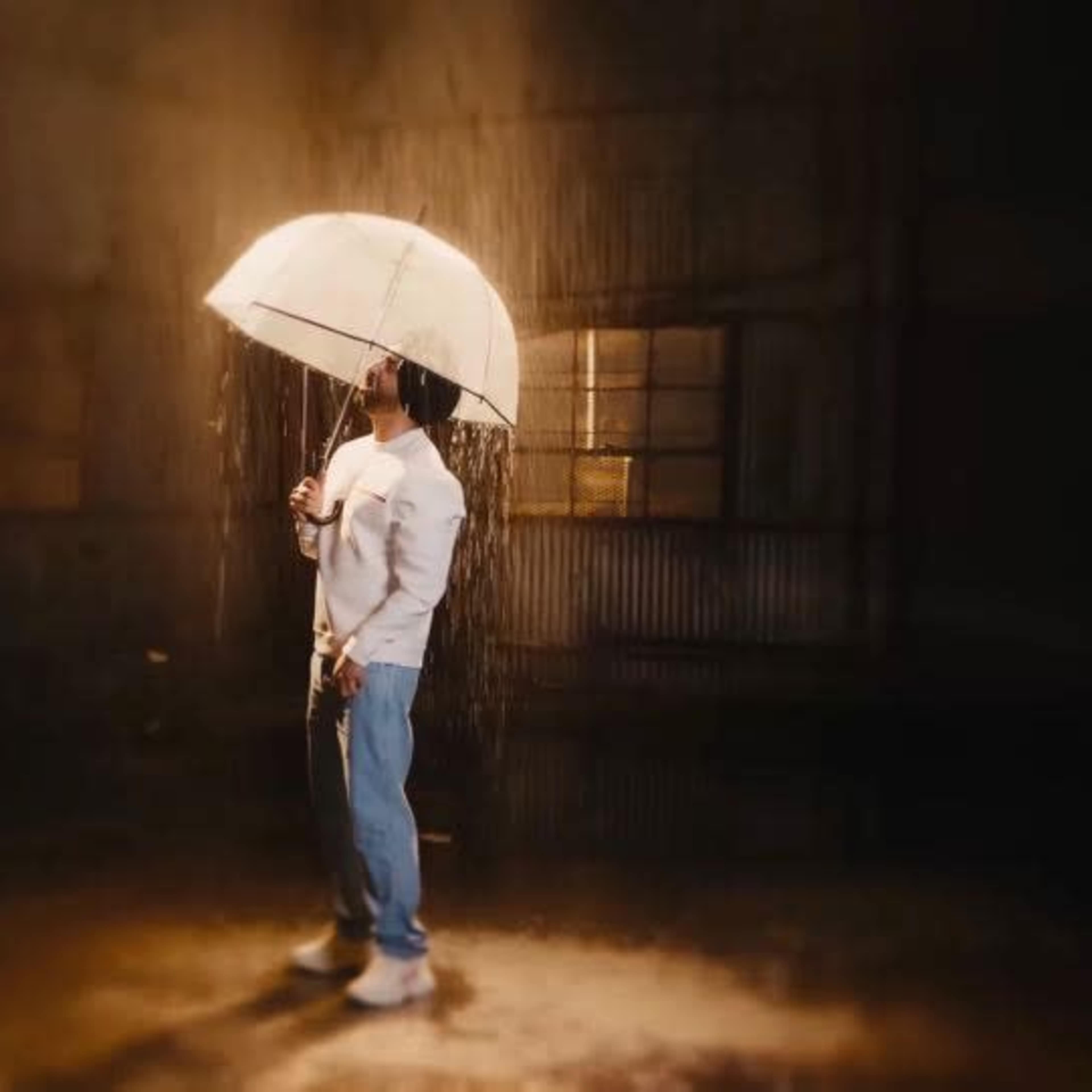 A person stands under an umbrella in a dimly lit space, with water cascading down around them.