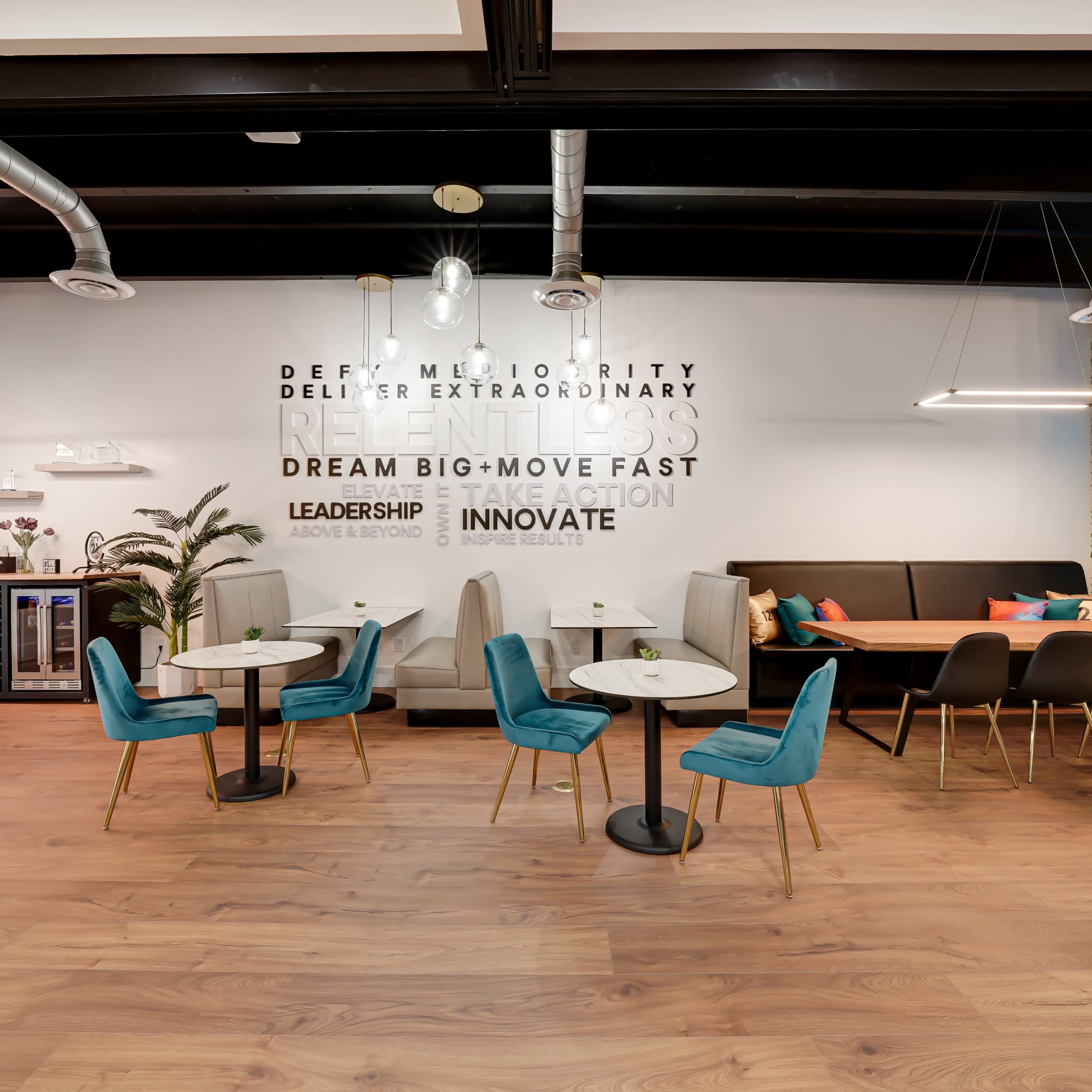 A modern coworking space with circular tables and teal chairs, a booth area, and motivational text on the walls.