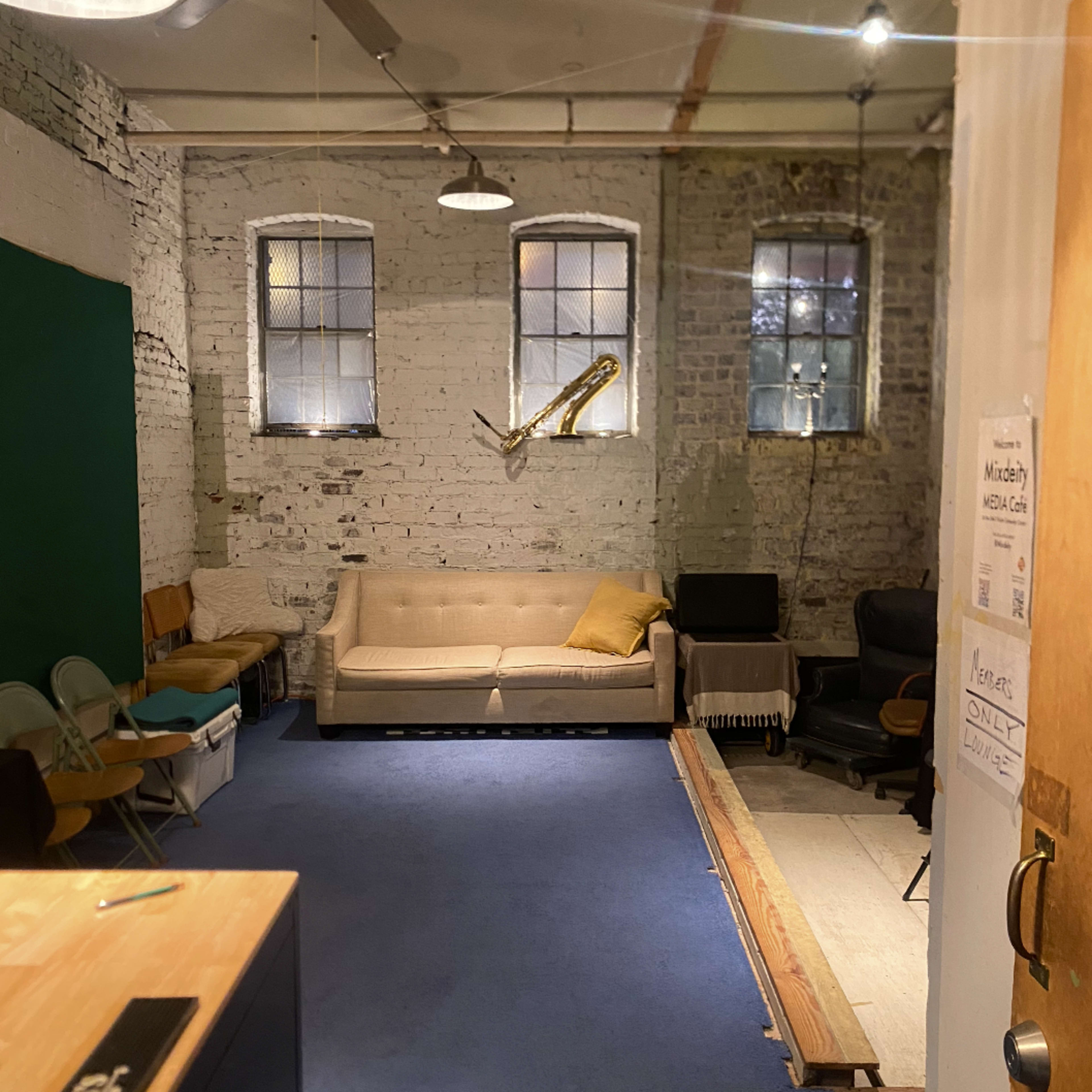 An interior room with exposed brick walls, a beige sofa, two windows, and a wooden door on the right.
