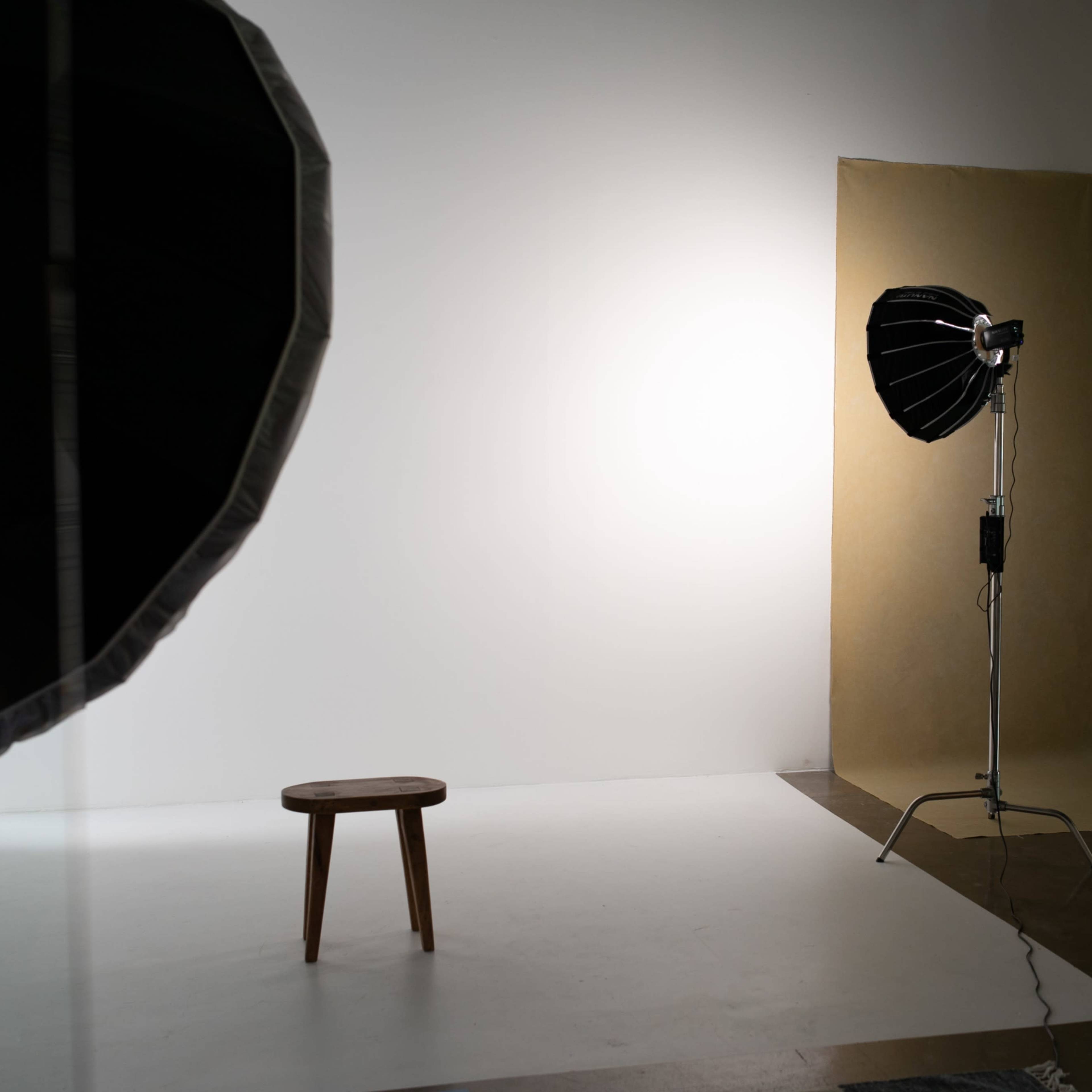A photography studio setup featuring a wooden stool, a backdrop, and studio lighting equipment.