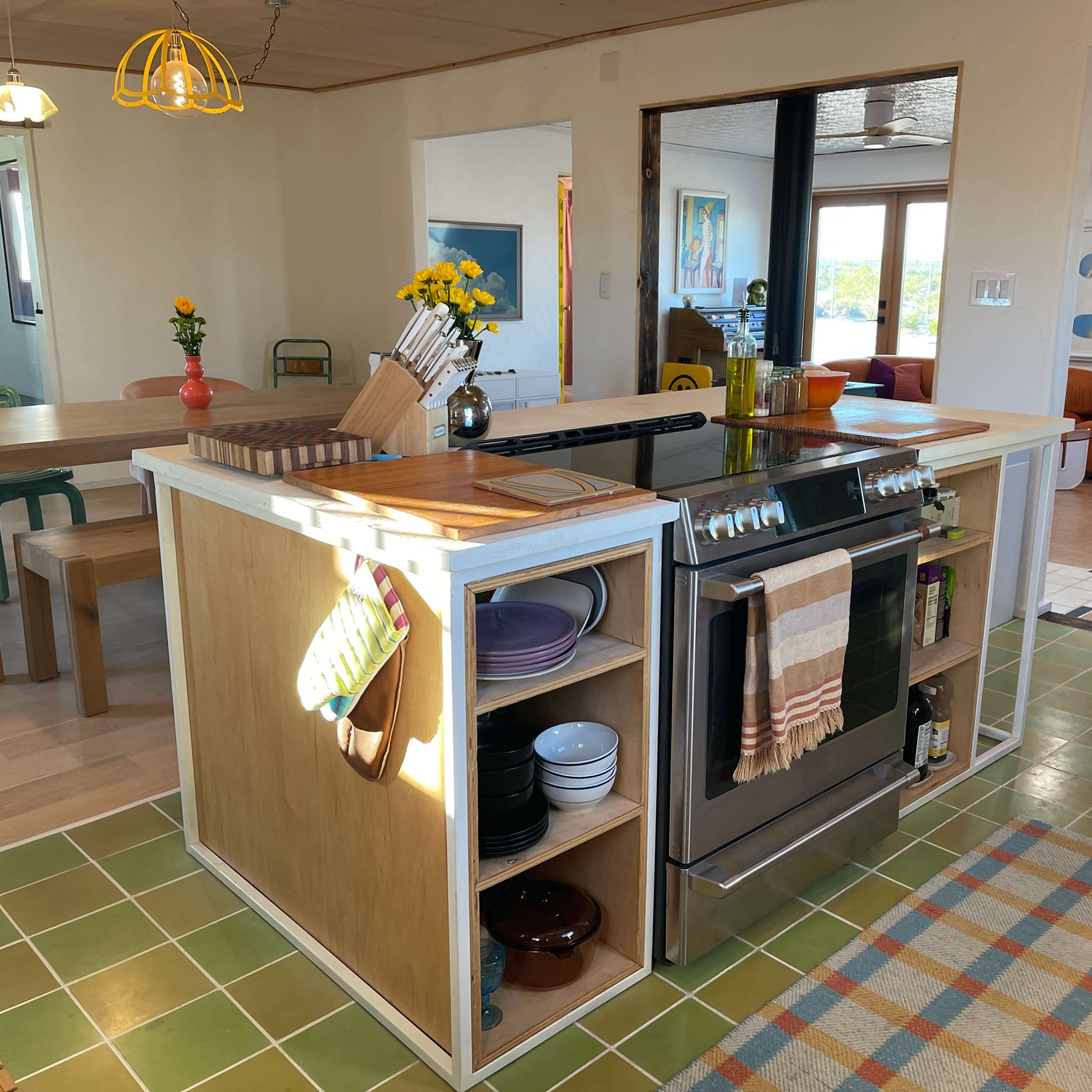 A modern kitchen with a large island featuring a stovetop, colorful dishes, and a dining area adjacent to it.