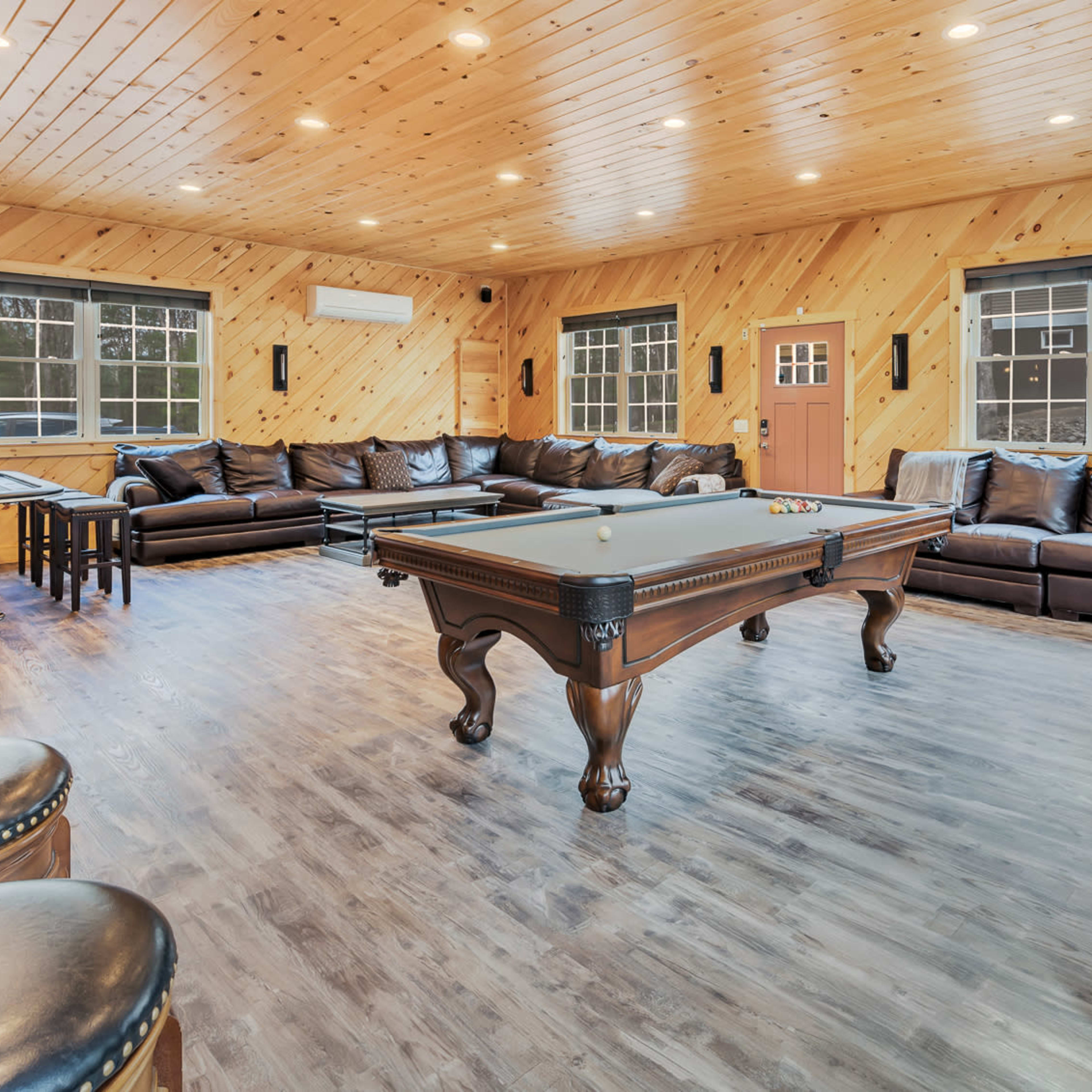 A large game room with a pool table, leather sofas, and wooden accents, illuminated by recessed lighting.