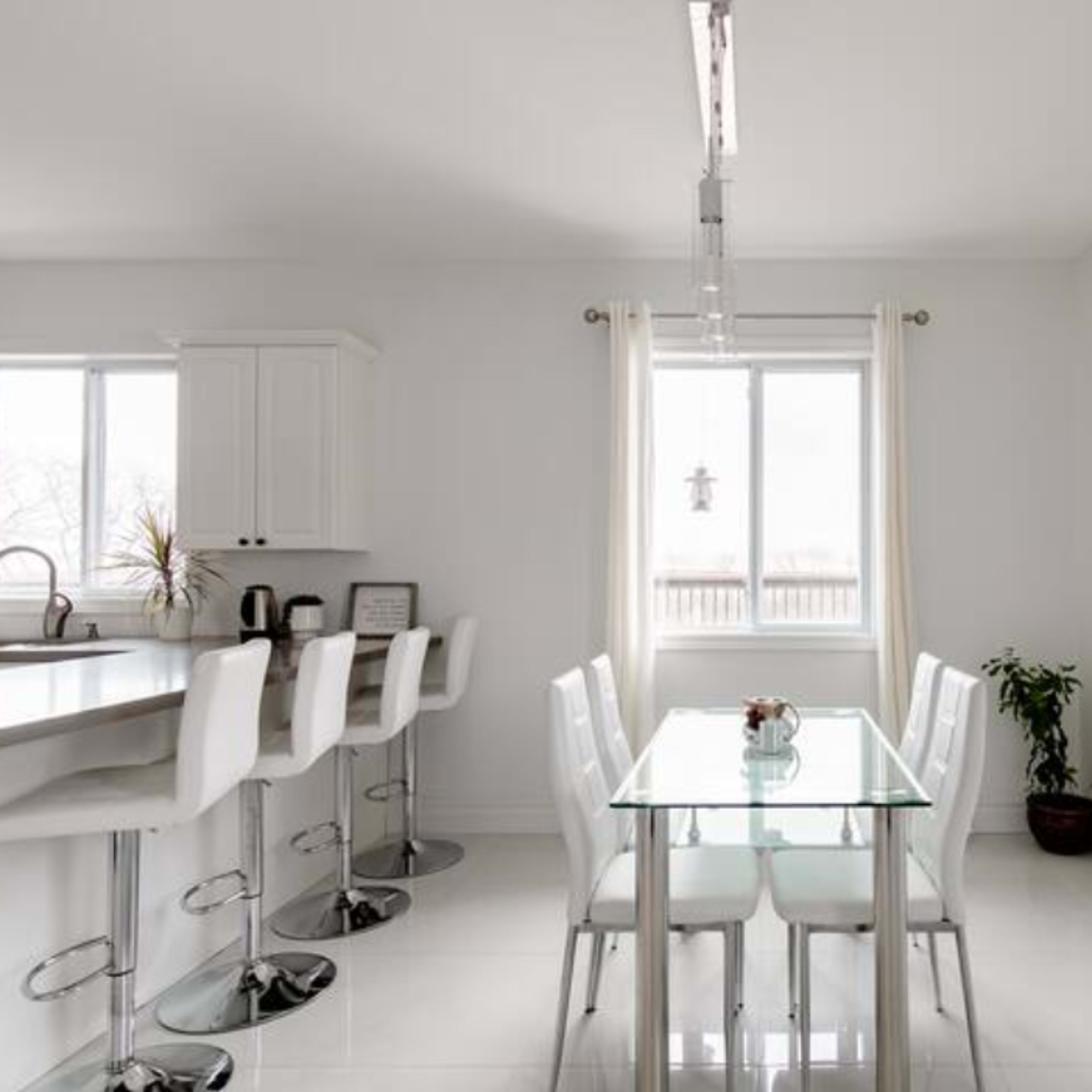 A modern kitchen and dining area featuring white cabinetry, a glass dining table with white chairs, and a large artwork on the wall.