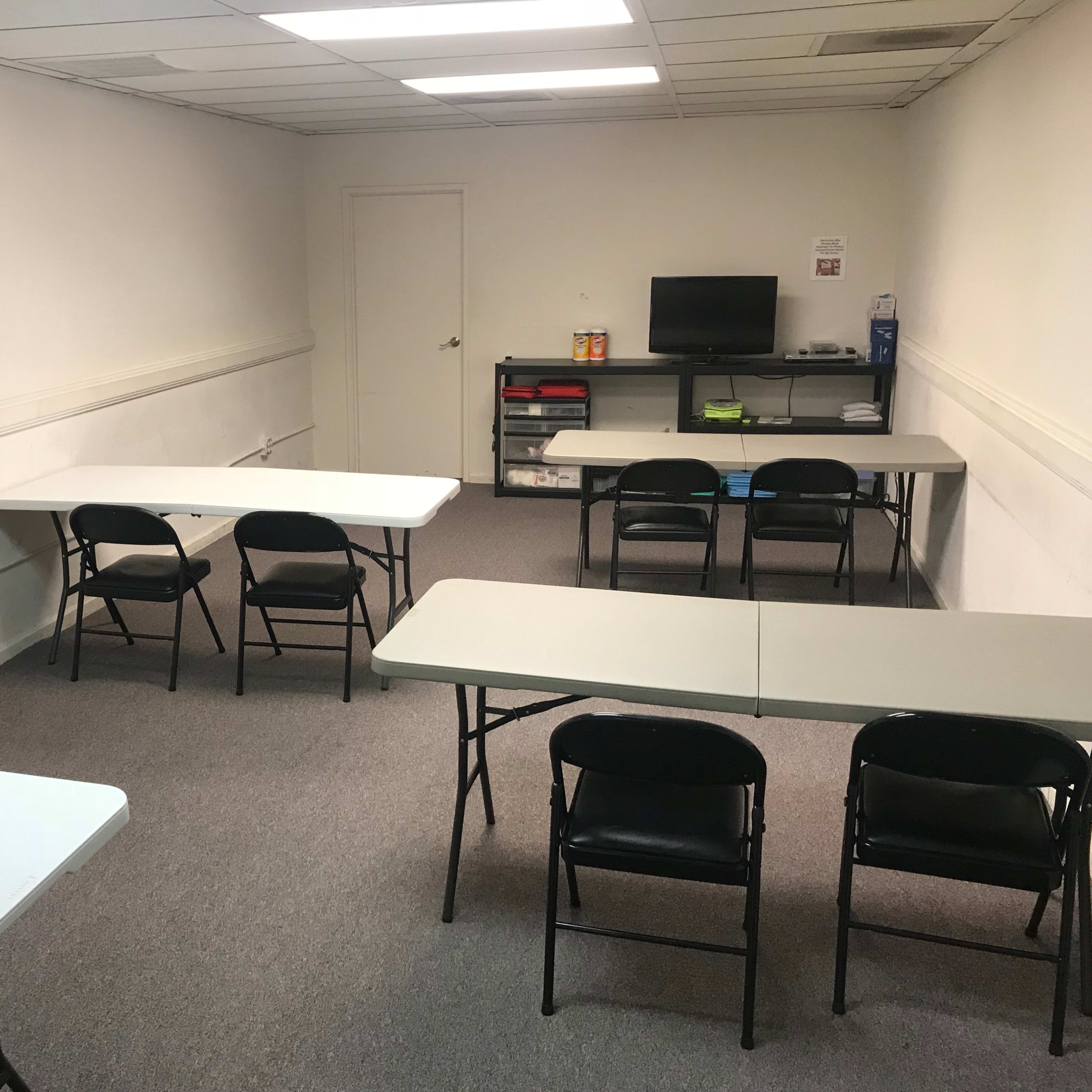 A bare room with several folding tables and chairs arranged, featuring a small television and storage area.