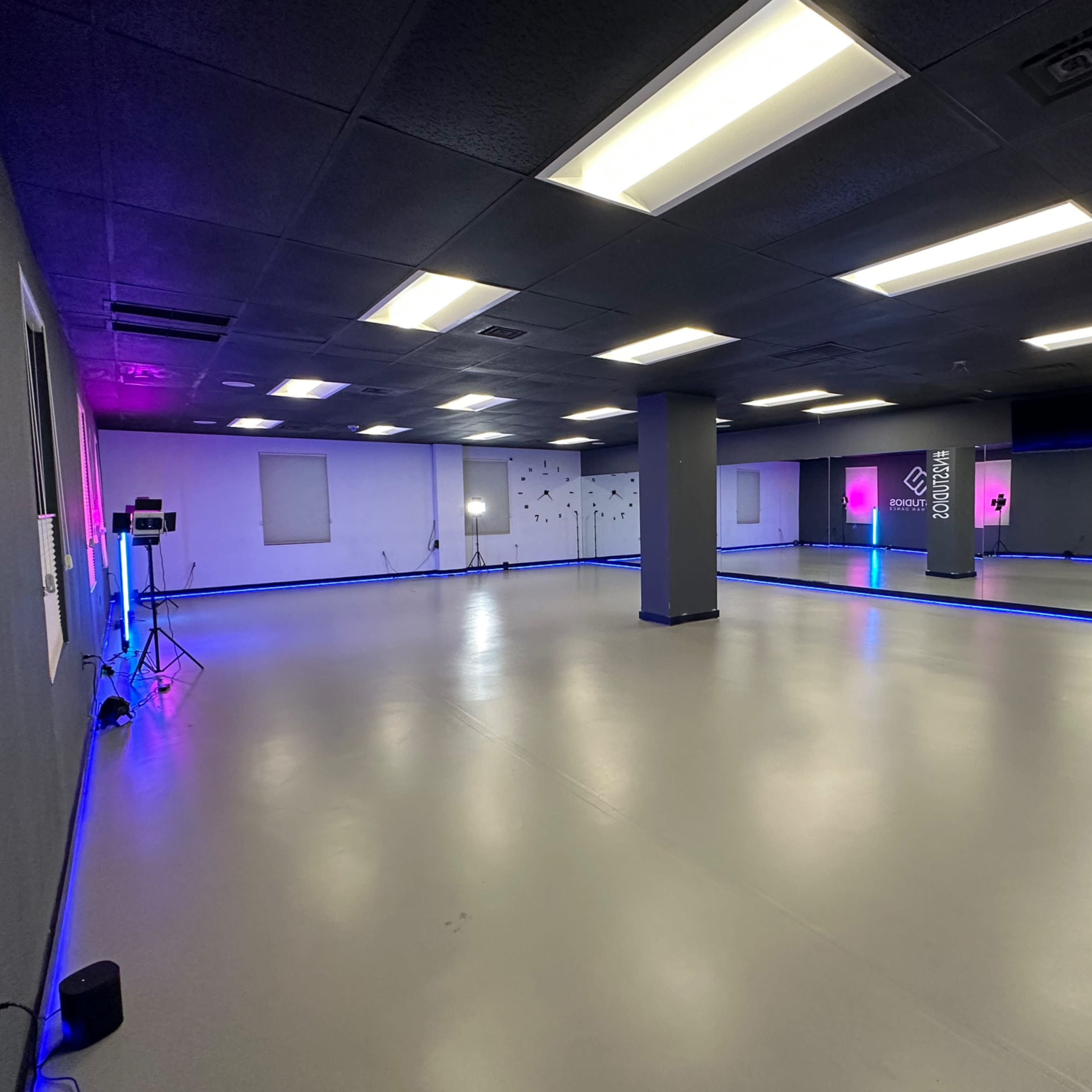 An empty dance studio with colorful LED lighting and a smooth, gray floor.