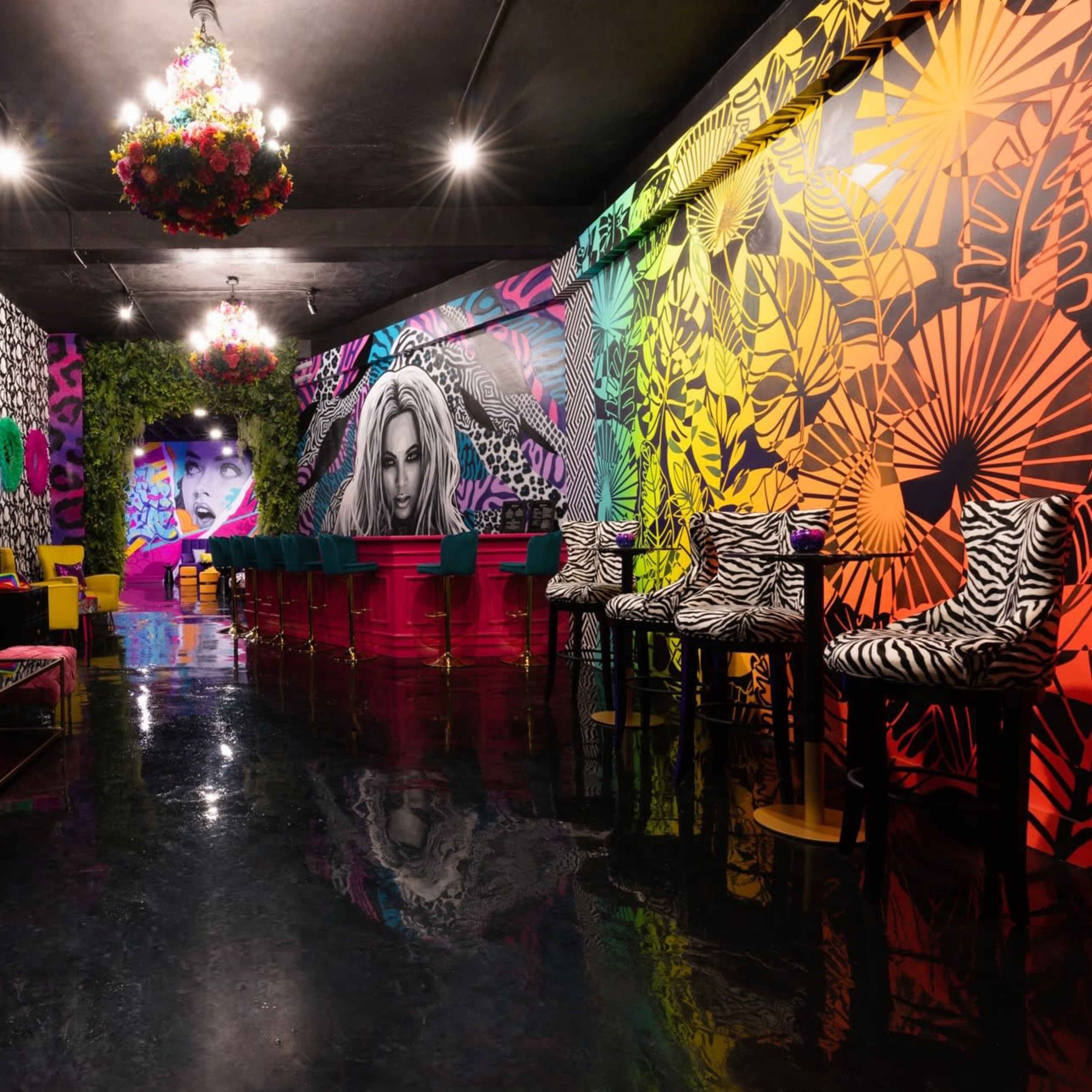 A vibrant lounge with bold, colorful murals of a lion and a woman's face, surrounded by stylish seating and a shiny black floor.
