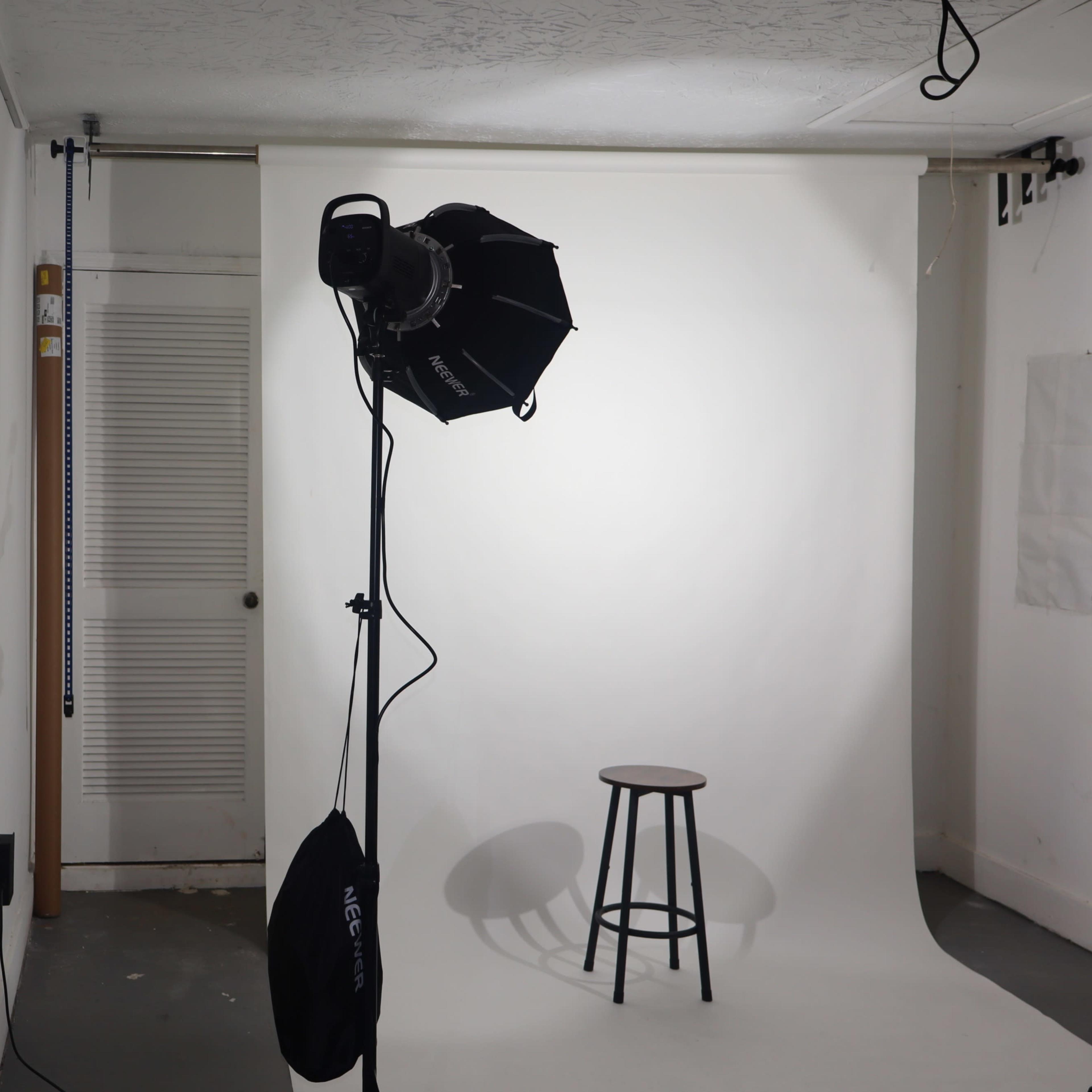 A photography studio setup with a mirror, a stool, and lighting equipment in front of a white backdrop.