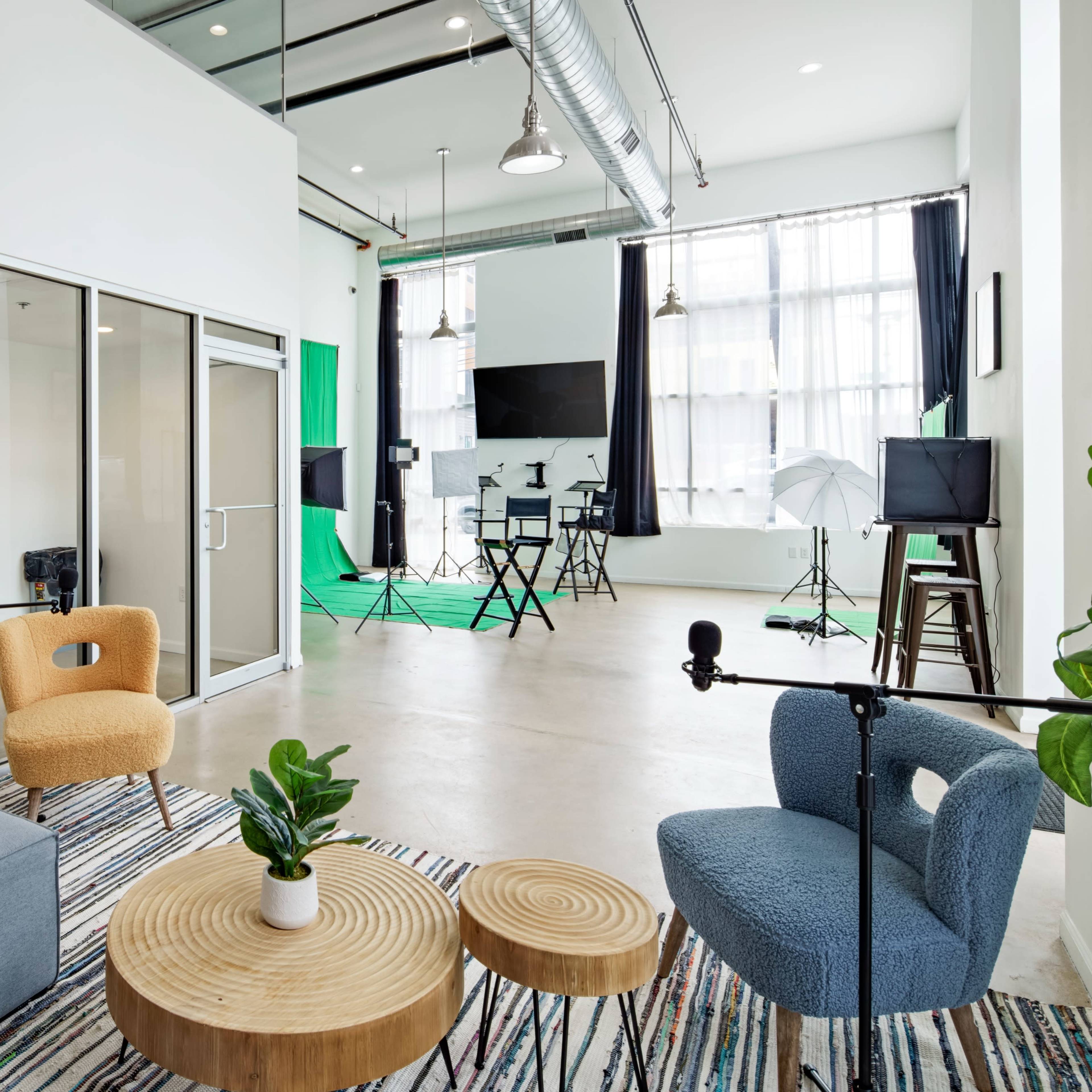 A spacious studio features modern furniture, a green screen setup, and equipment for video production.