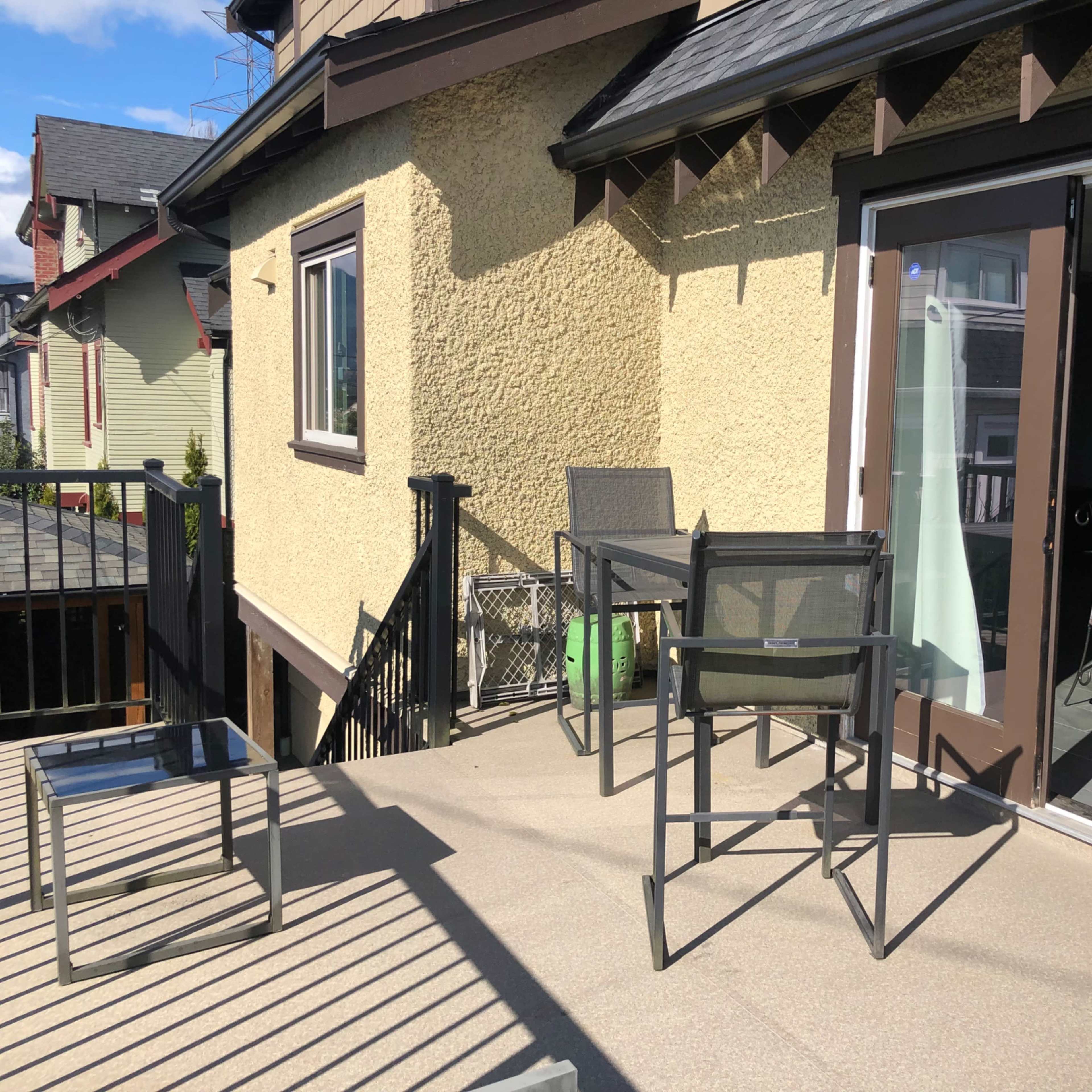 A balcony area with metal furniture, including two chairs and a small table, overlooking nearby houses.
