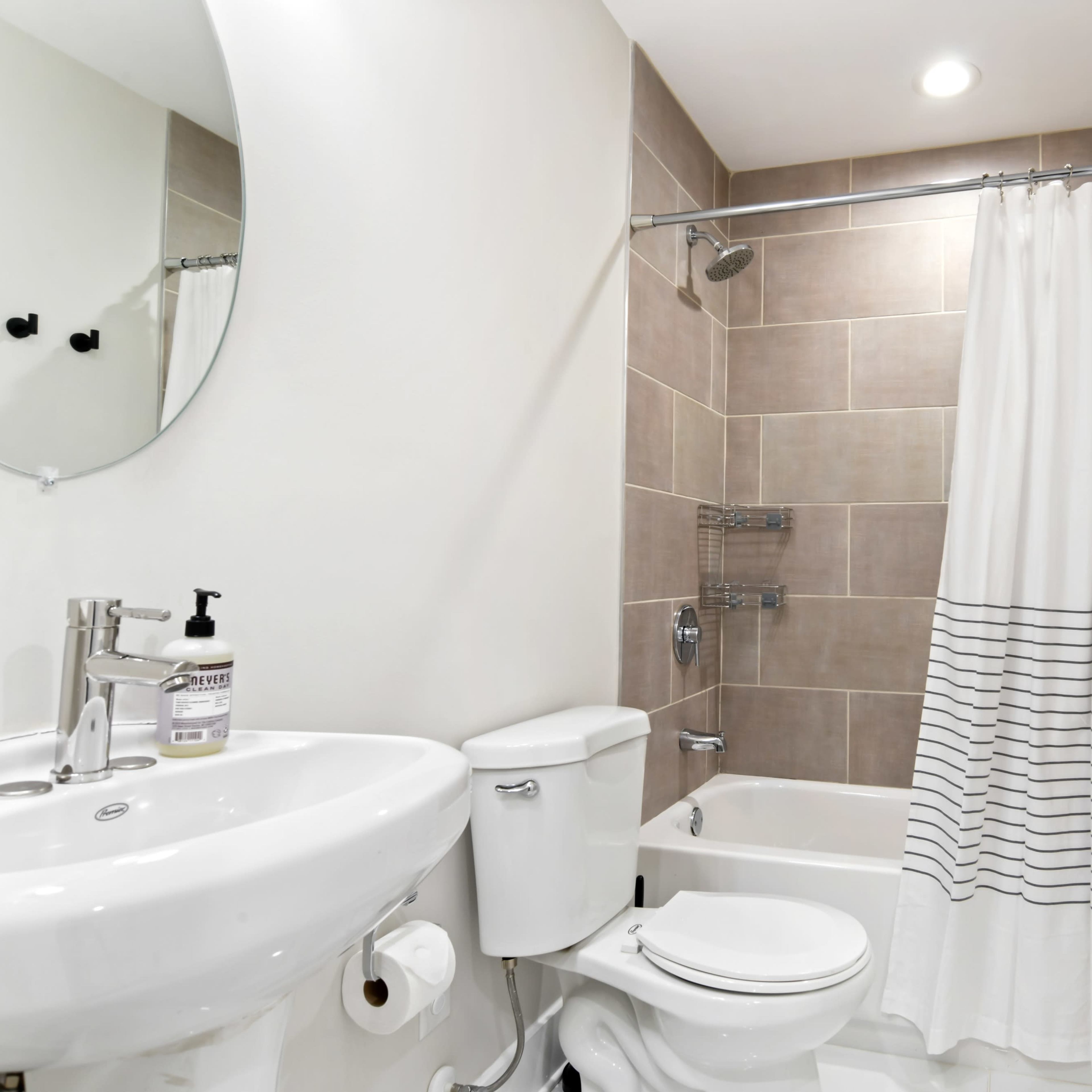 A clean bathroom features a white toilet, a sink with a faucet, a bathtub with a shower curtain, and tiled walls.
