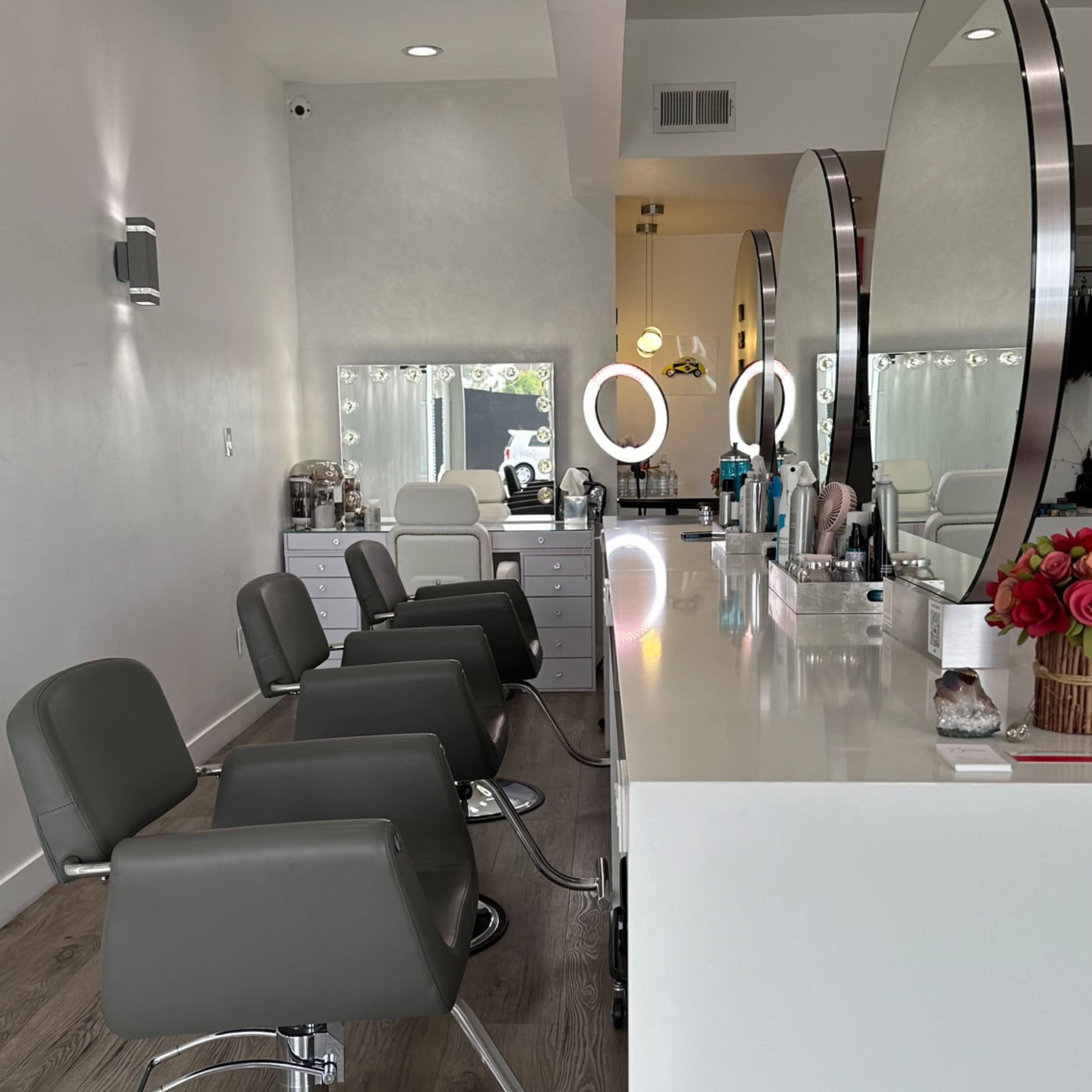 A modern hair salon with several gray salon chairs in front of a white countertop and large mirrors.