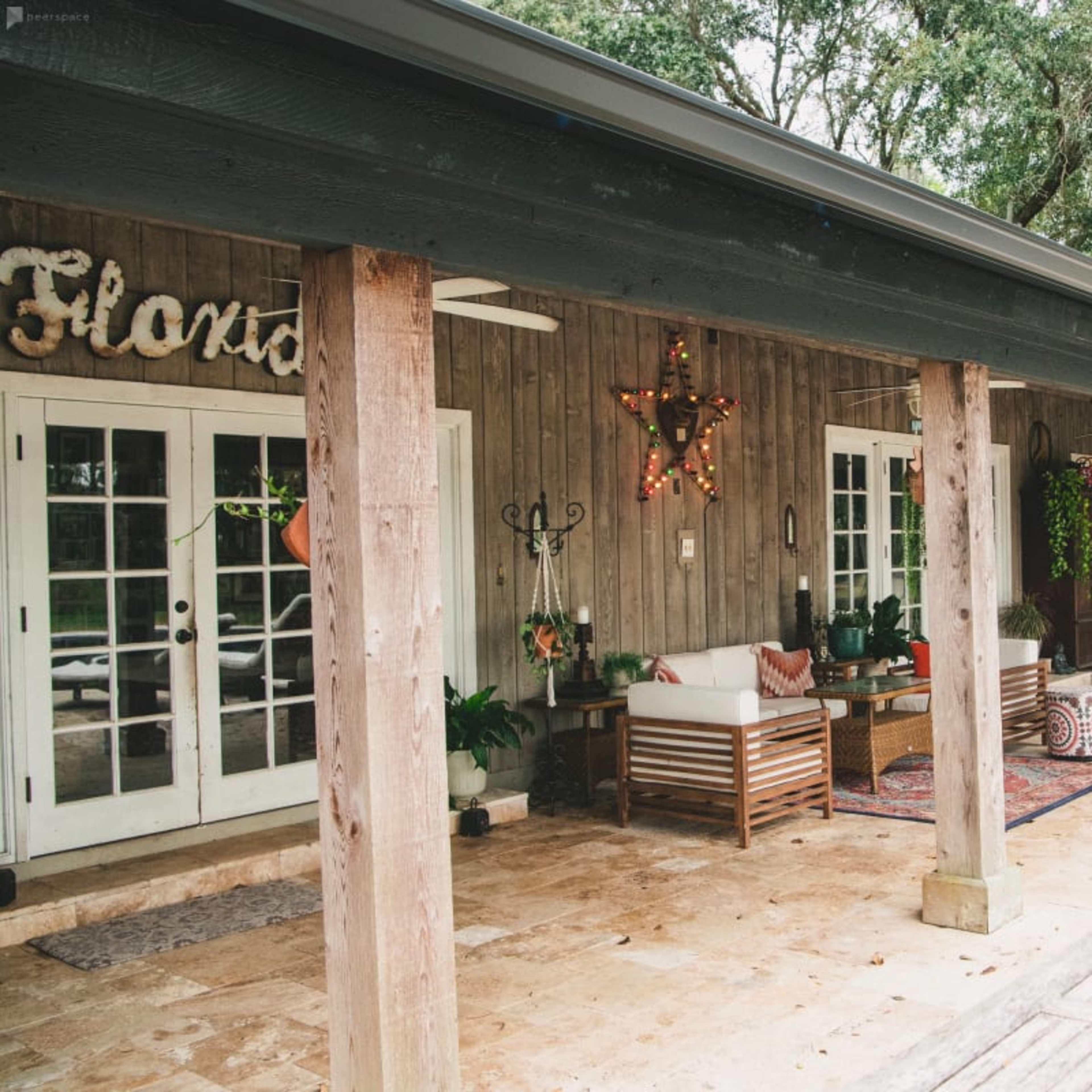 A covered outdoor patio with wooden posts, seating arrangements, and decorative elements surrounded by trees.